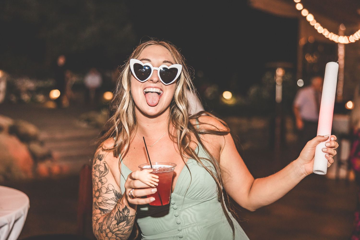 Party guests celebrating with drinks under warm string lights at evening reception.