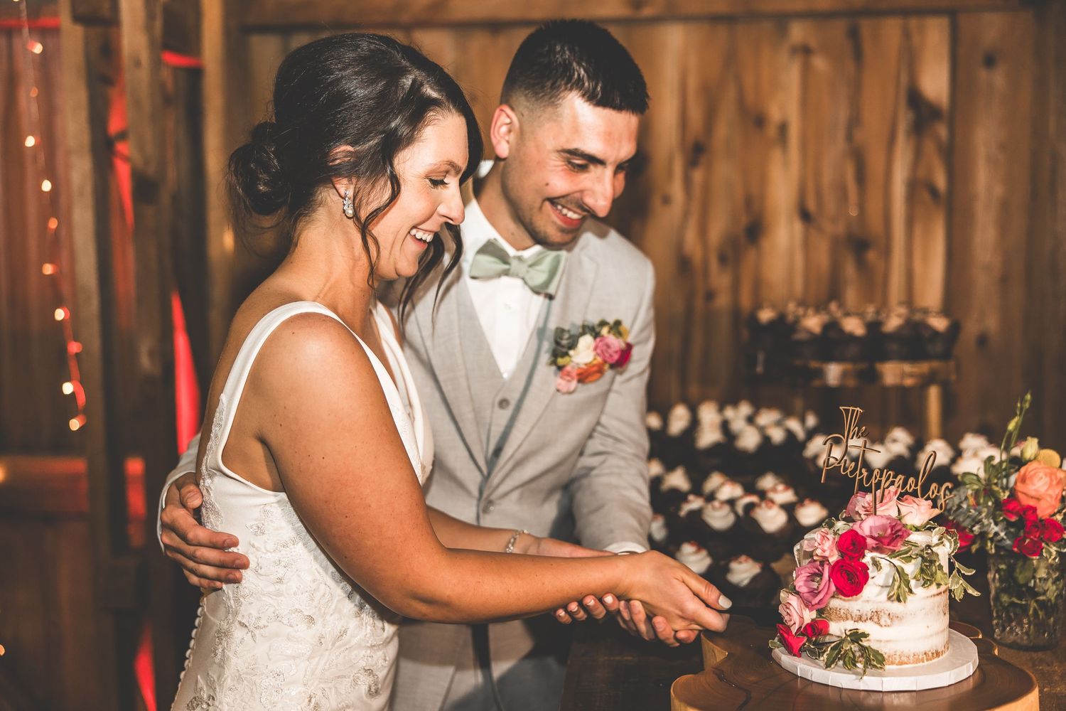 A joyful moment shared while cutting the wedding cake in a rustic barn setting.