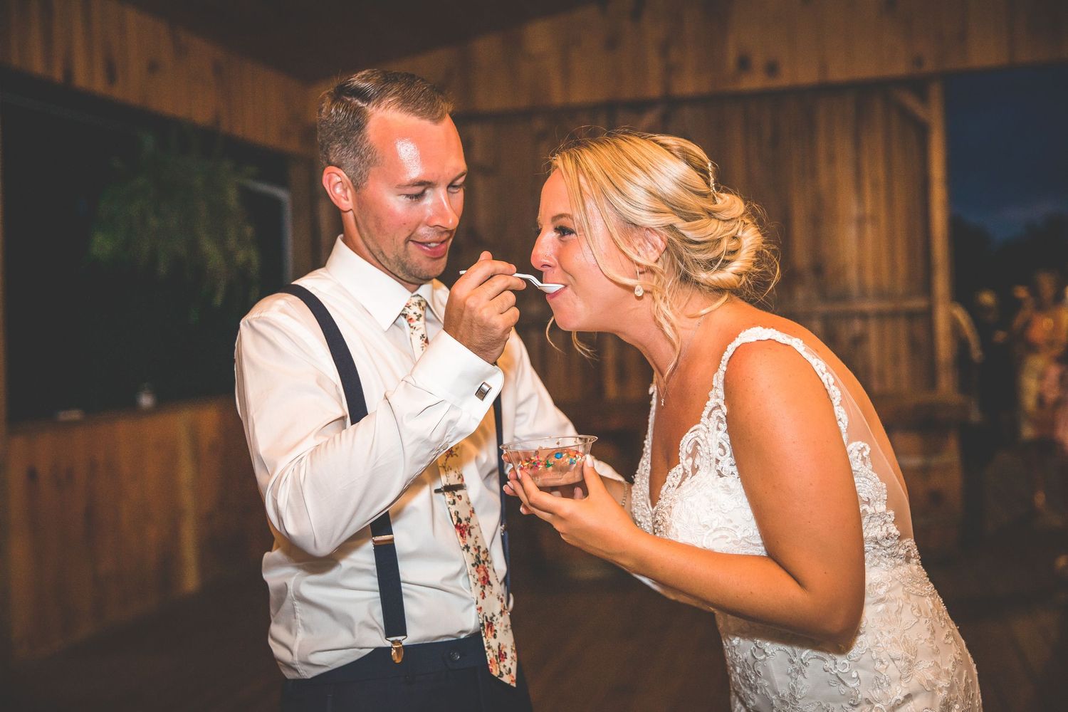 A couple sharing a playful moment while eating cake at their rustic barn reception.