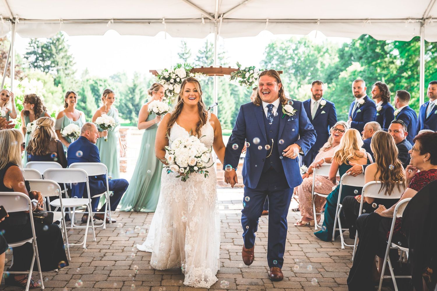 Guests mingling and celebrating at an outdoor wedding reception under a white tent.