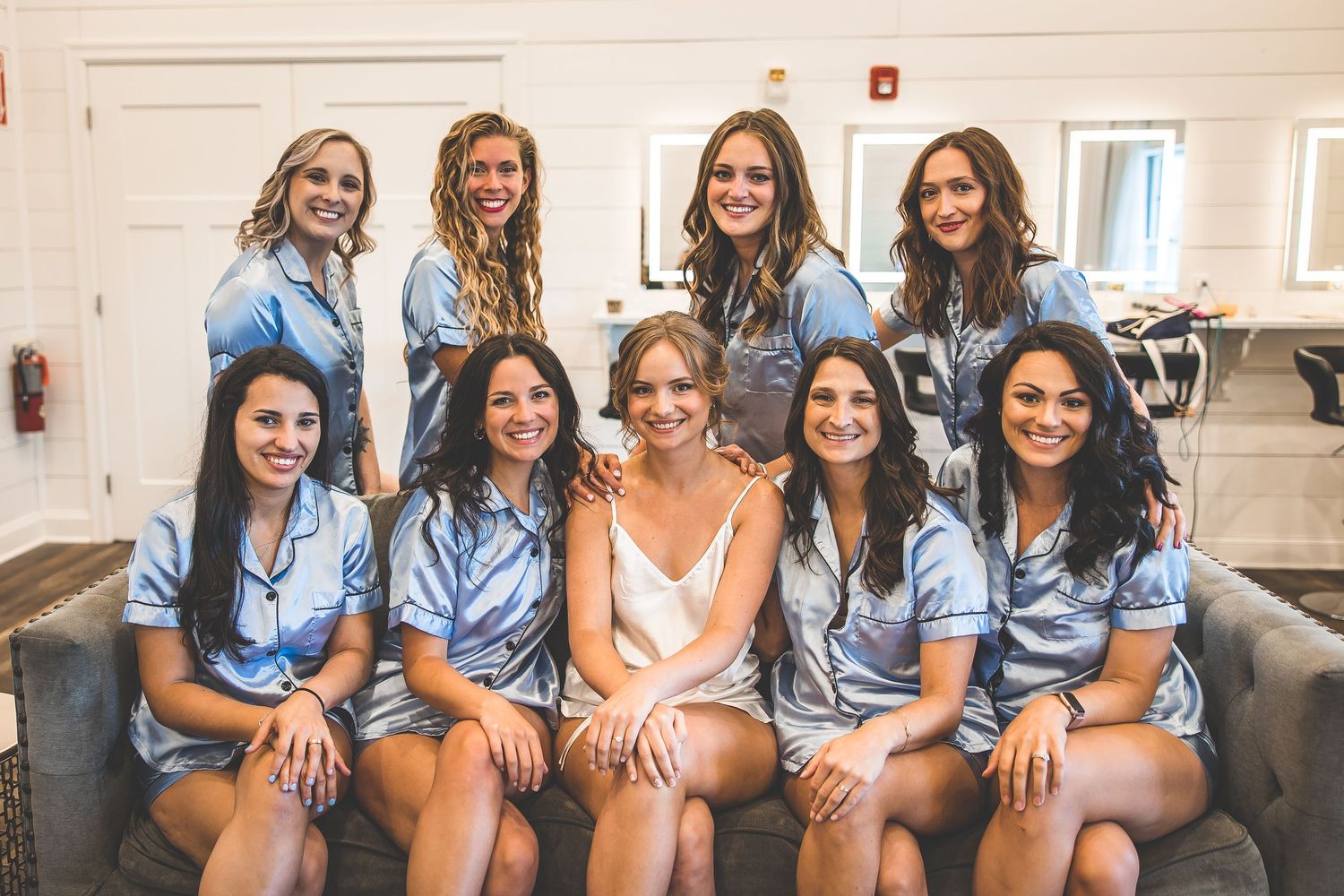 Bridesmaids wearing light blue dresses pose together on a couch.