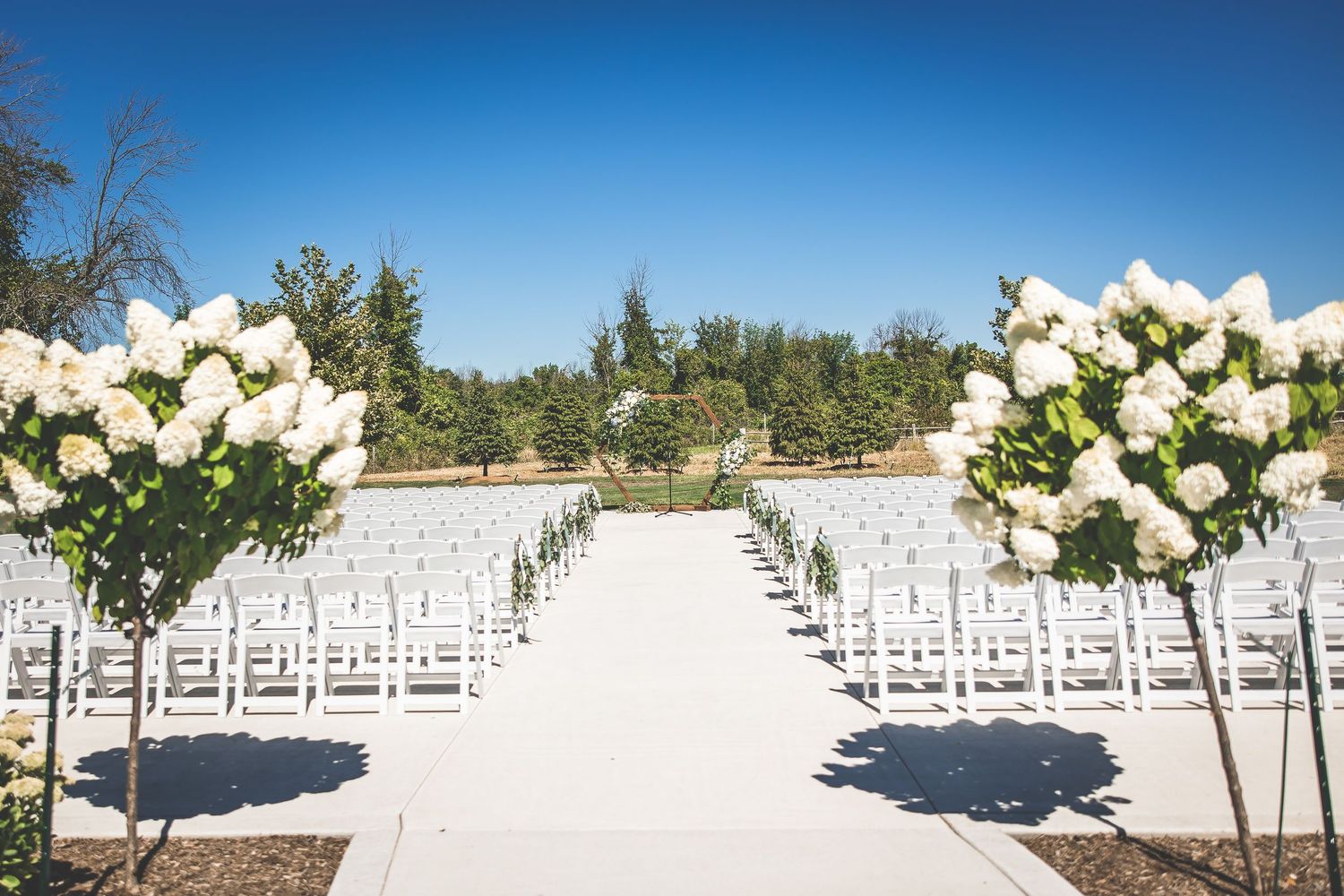 Outdoor wedding ceremony setup with rows of white chairs and floral decorations.
