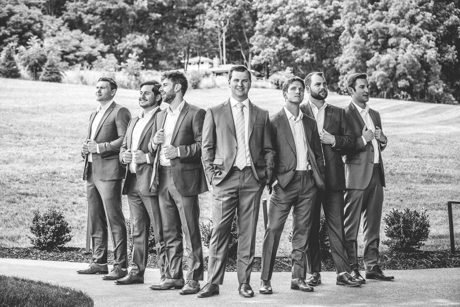 Black and white photo of groomsmen in matching attire standing in a line outdoors.
