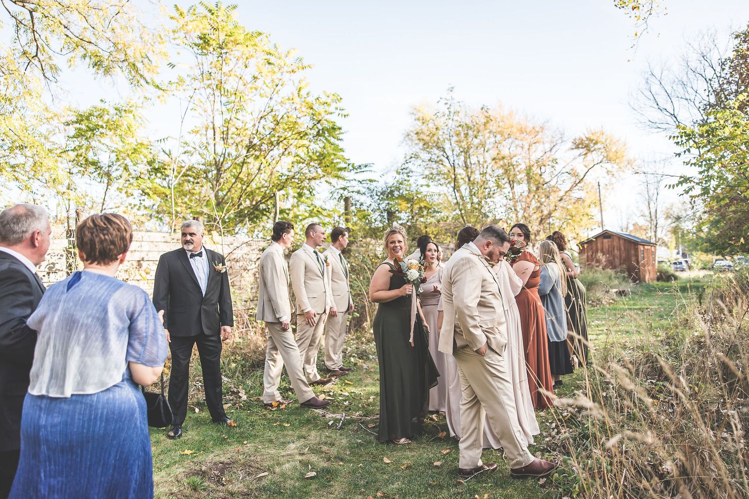 Wedding guests standing in outdoor ceremony space surrounded by autumn trees.