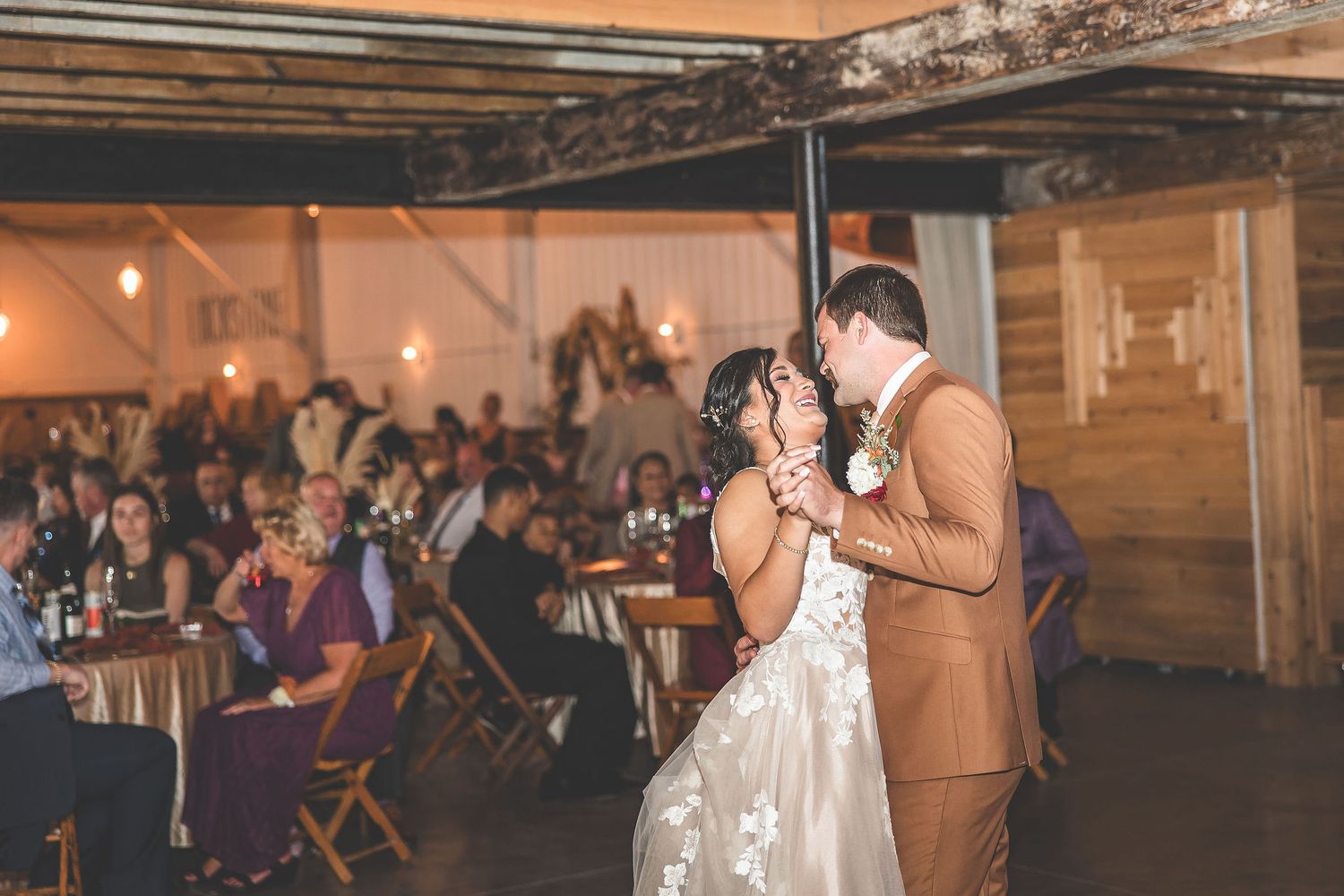 Wedding guests watch as a couple shares their first dance in a rustic barn reception space.