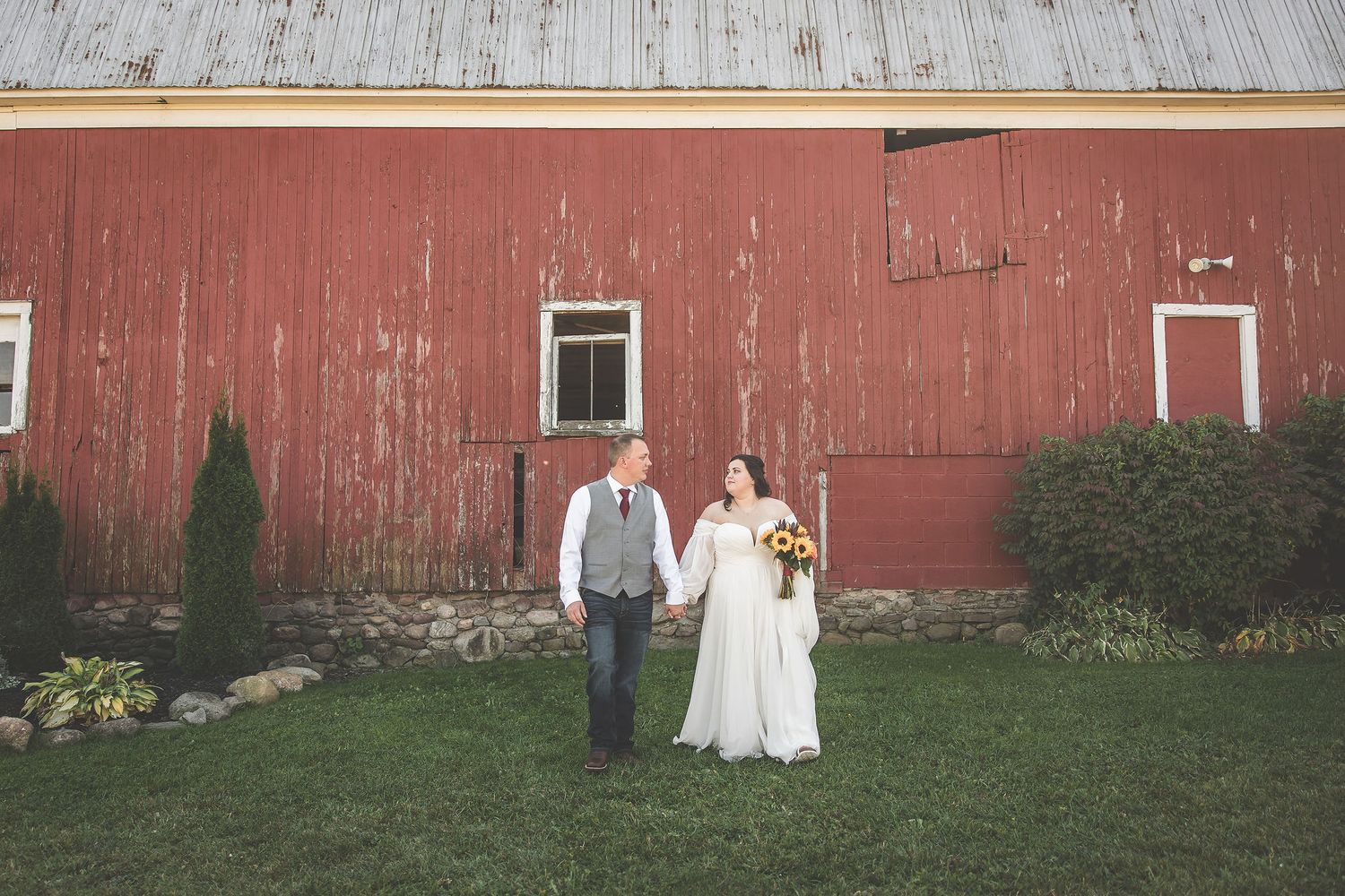 Wedding couple photographed against weathered barn in rural setting.