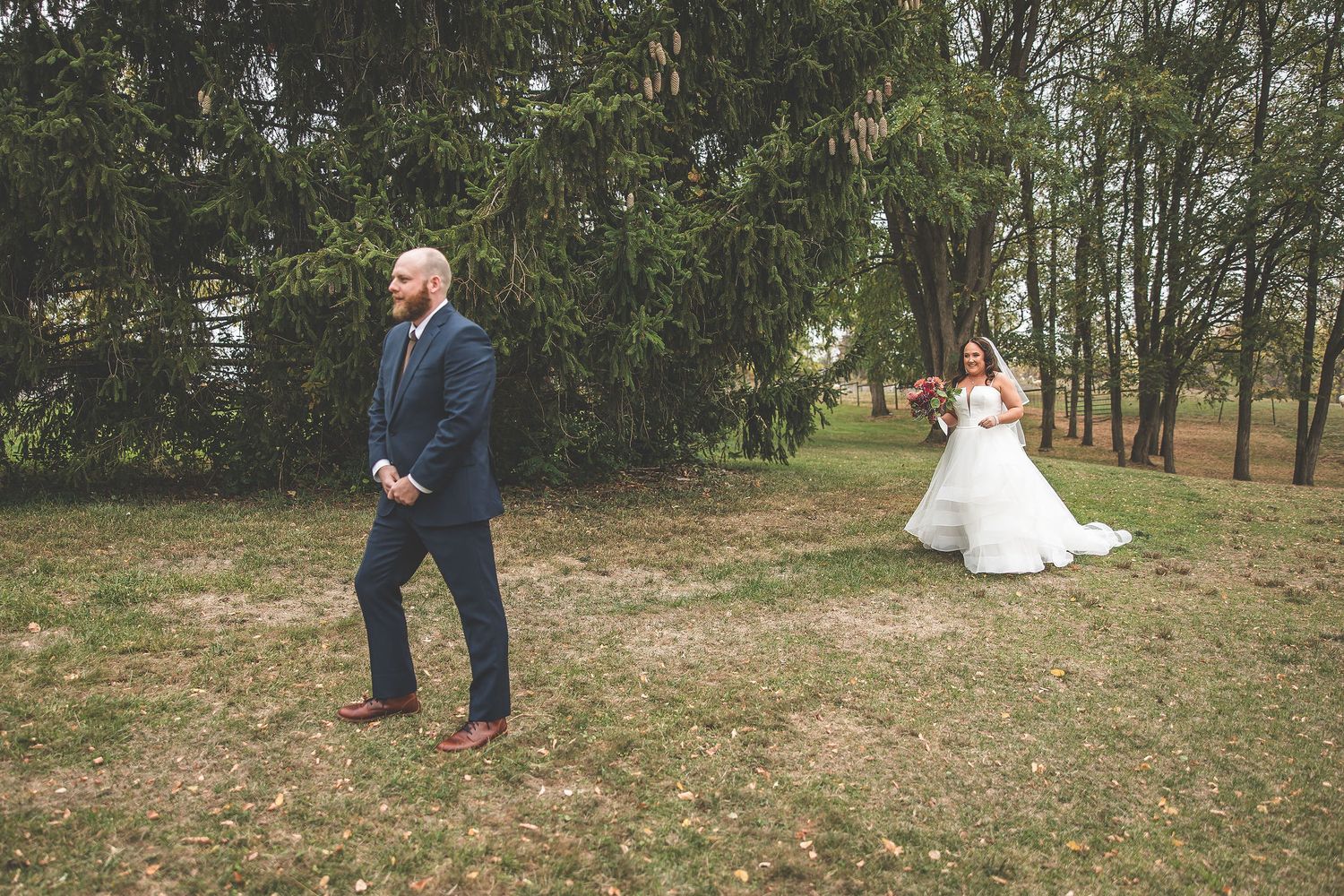 A wedding photoshoot in a natural outdoor setting with evergreen trees and fallen leaves.