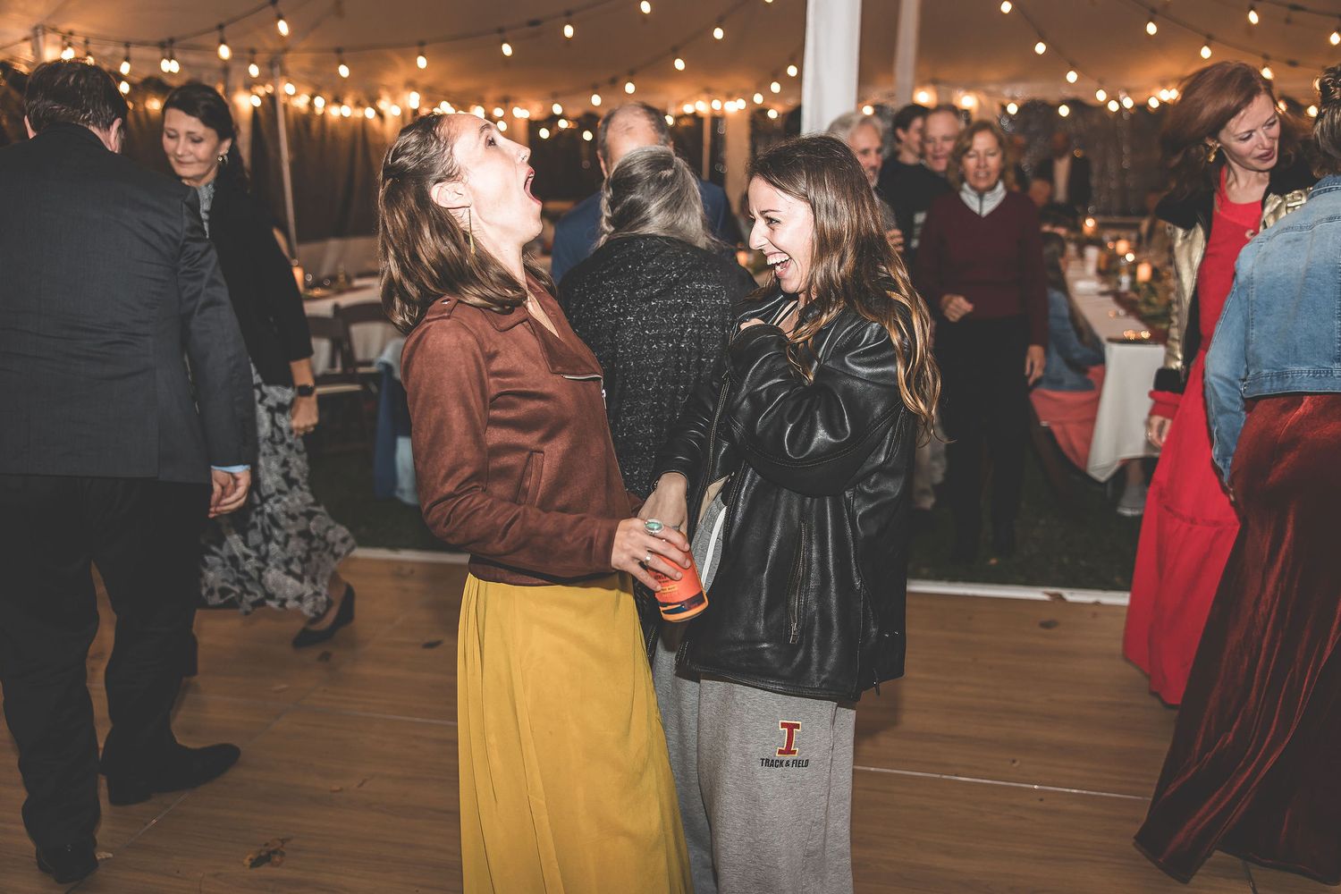 Wedding party members and guests enjoying themselves on a lively dance floor with string lighting above.