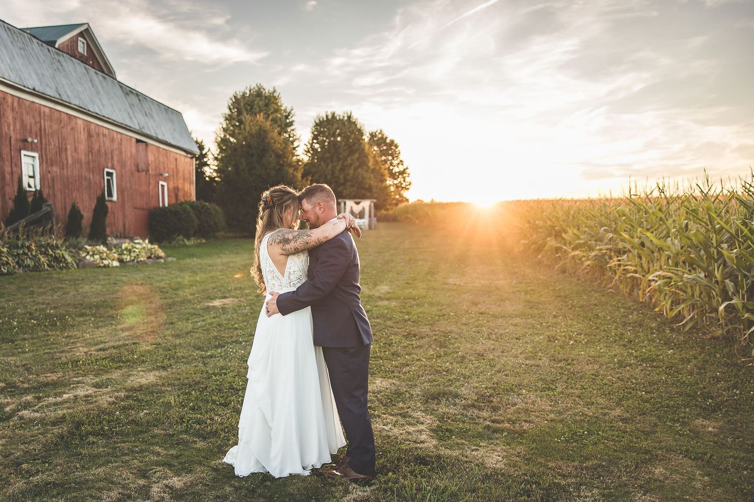 Couple dancing together outside red barn during sunset wedding photoshoot.