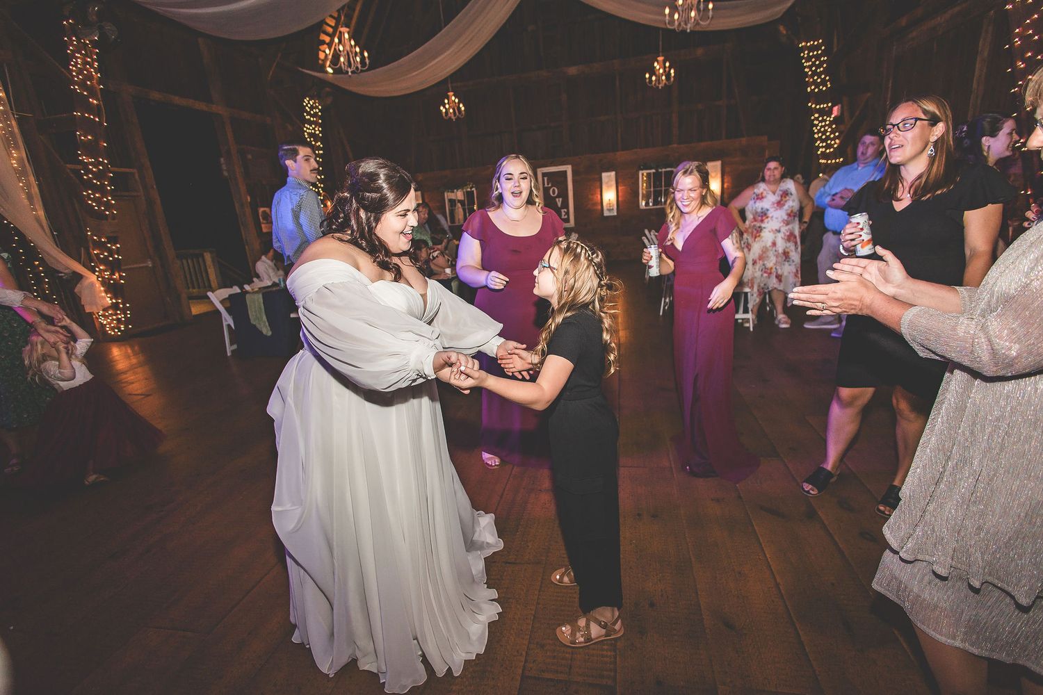 Wedding celebration with guests dancing in a rustic venue decorated with soft lighting.