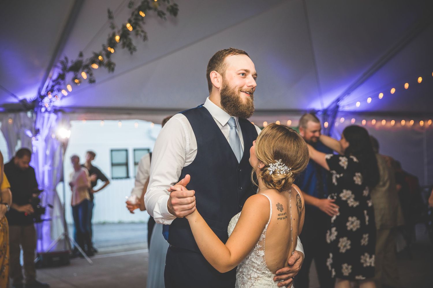 Wedding reception dance floor filled with guests under twinkling lights in an outdoor tent.