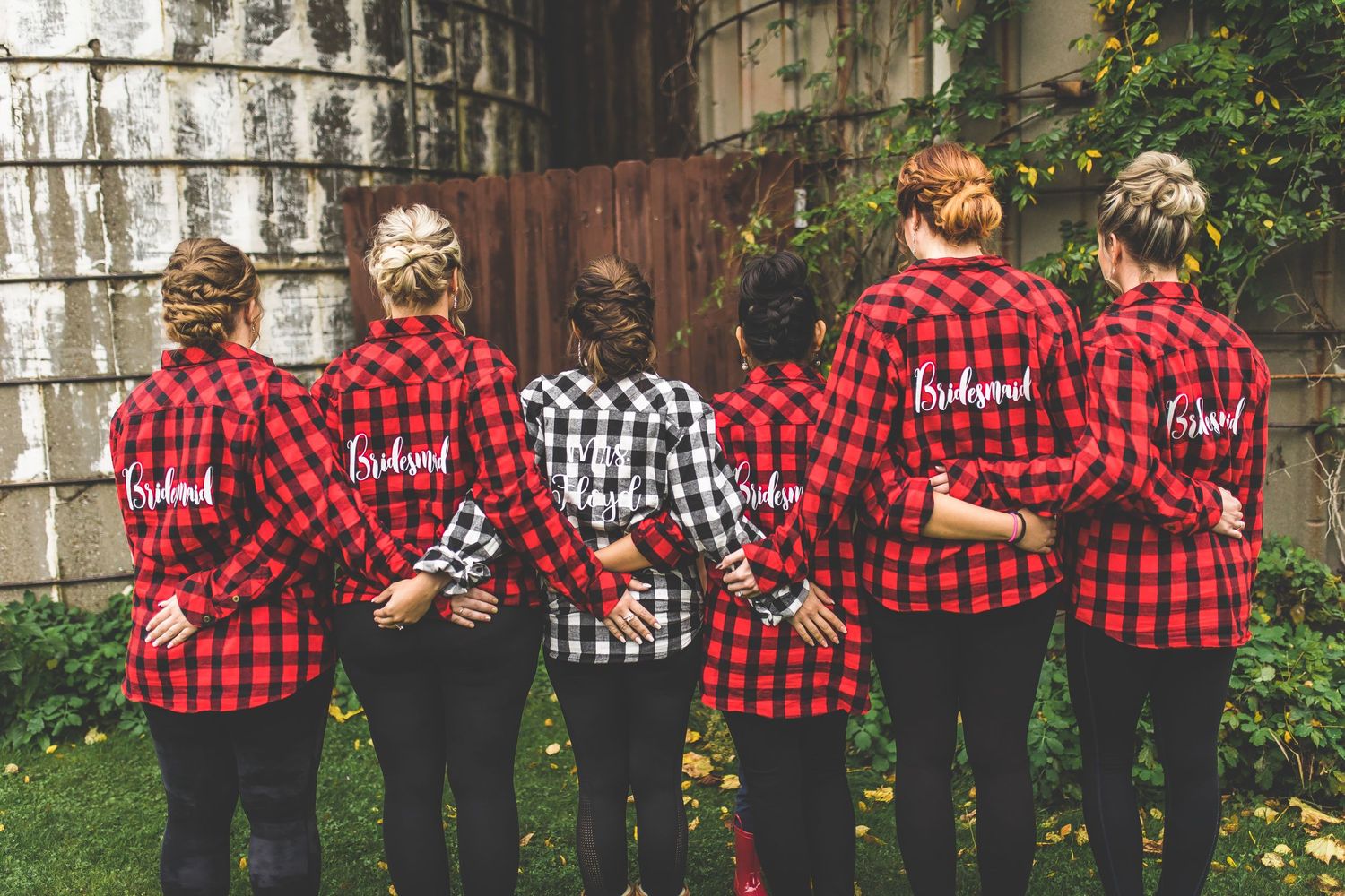 Line of friends in matching red and black buffalo plaid shirts posing against outdoor wall.