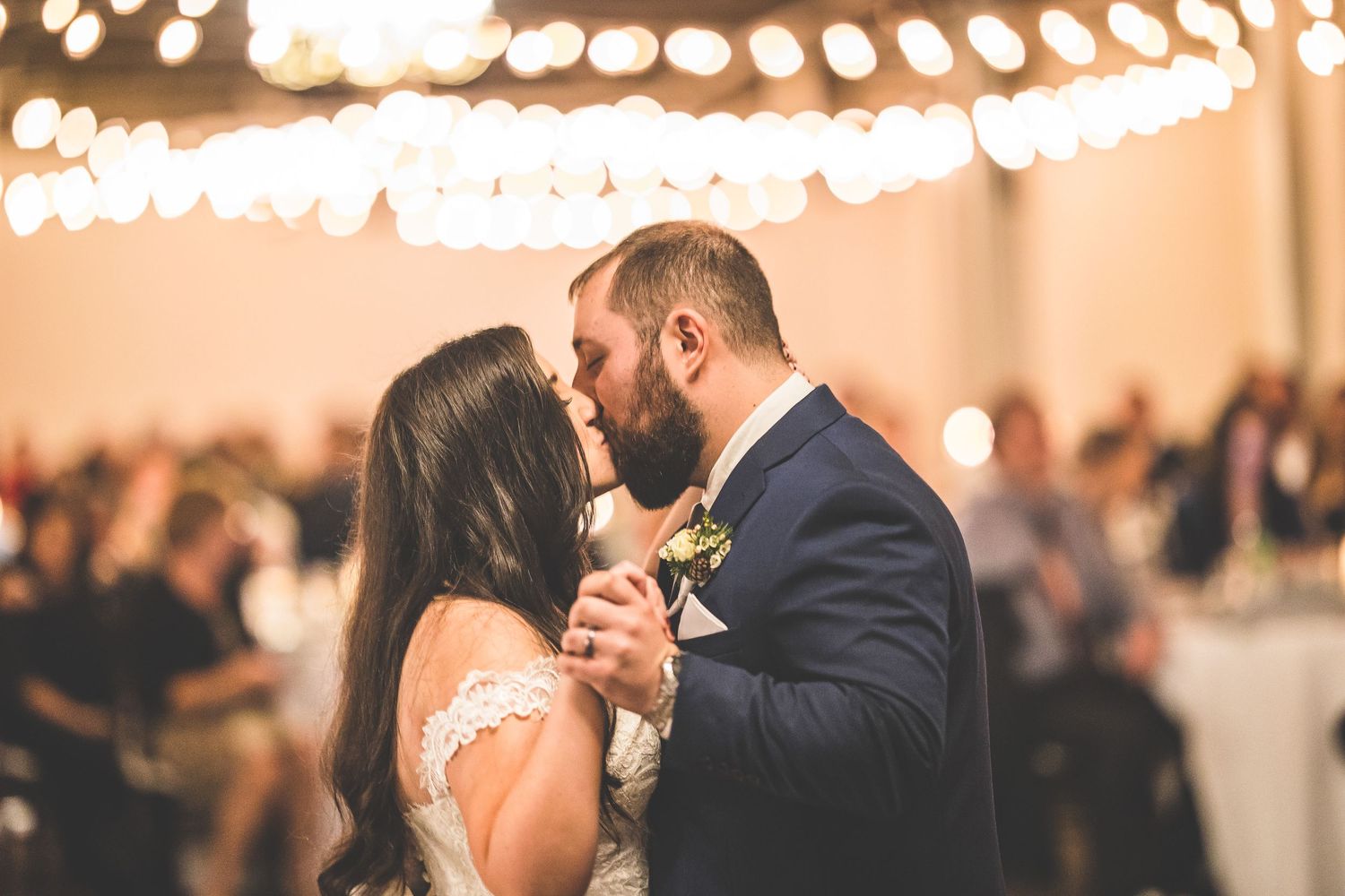 Romantic dance moment captured under warm string lights at an indoor wedding reception.