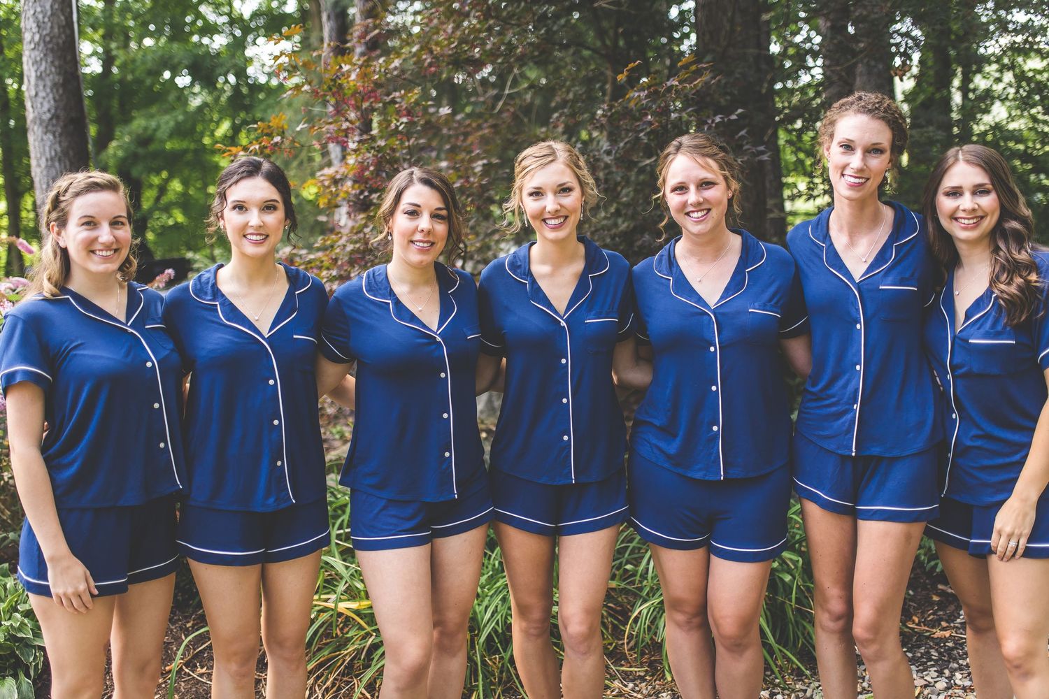 Bridesmaids in matching navy blue robes lined up outdoors for a group photo.