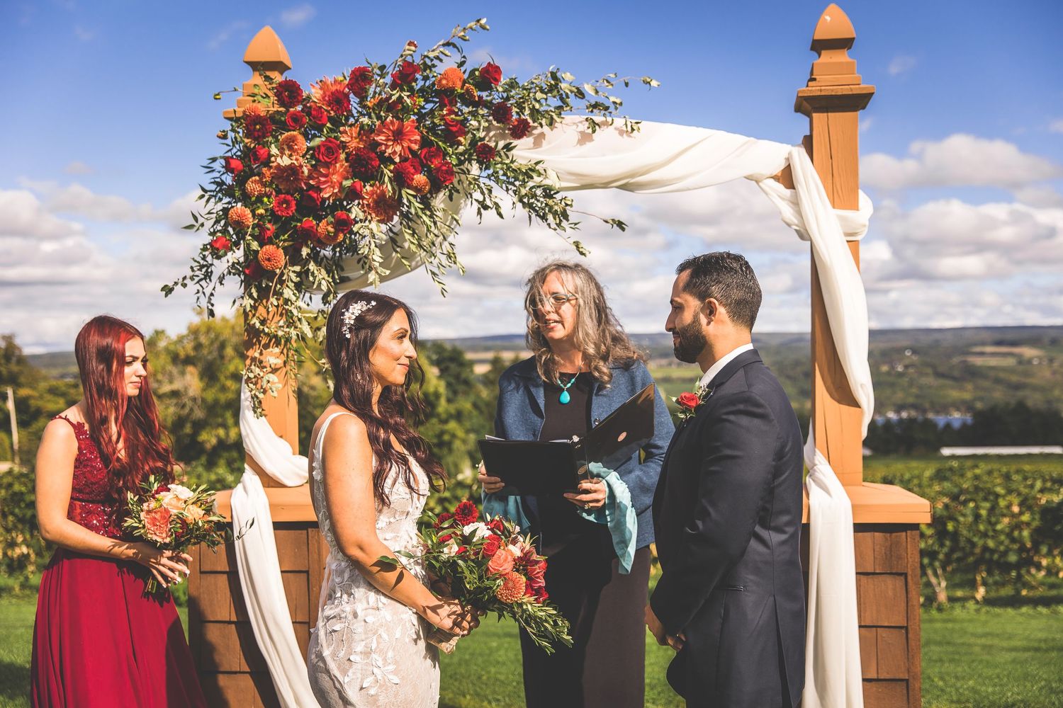 Outdoor wedding ceremony setup with wooden posts and vibrant red floral arrangements.