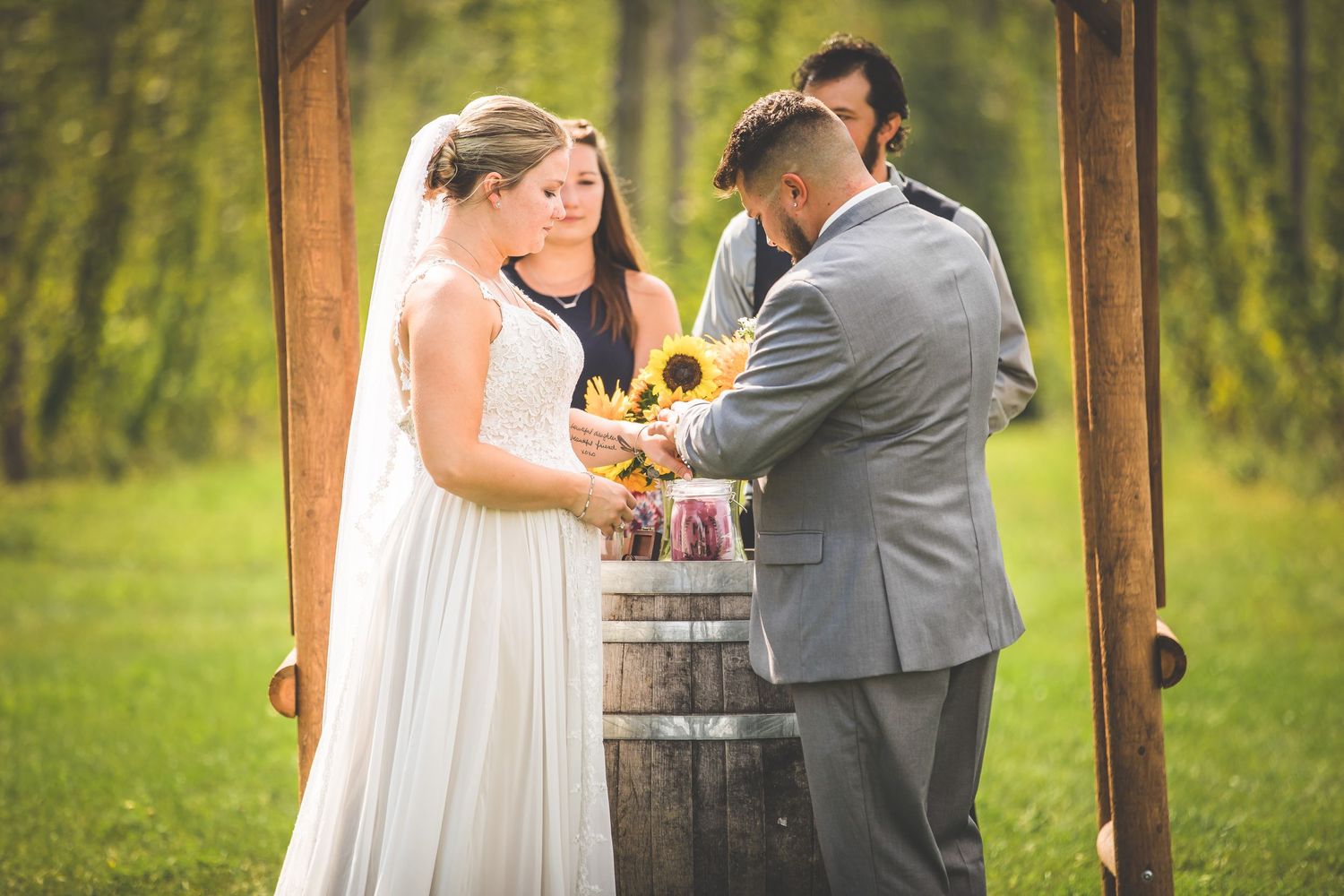 Intimate wedding ceremony moment at rustic wooden barrel altar surrounded by greenery.