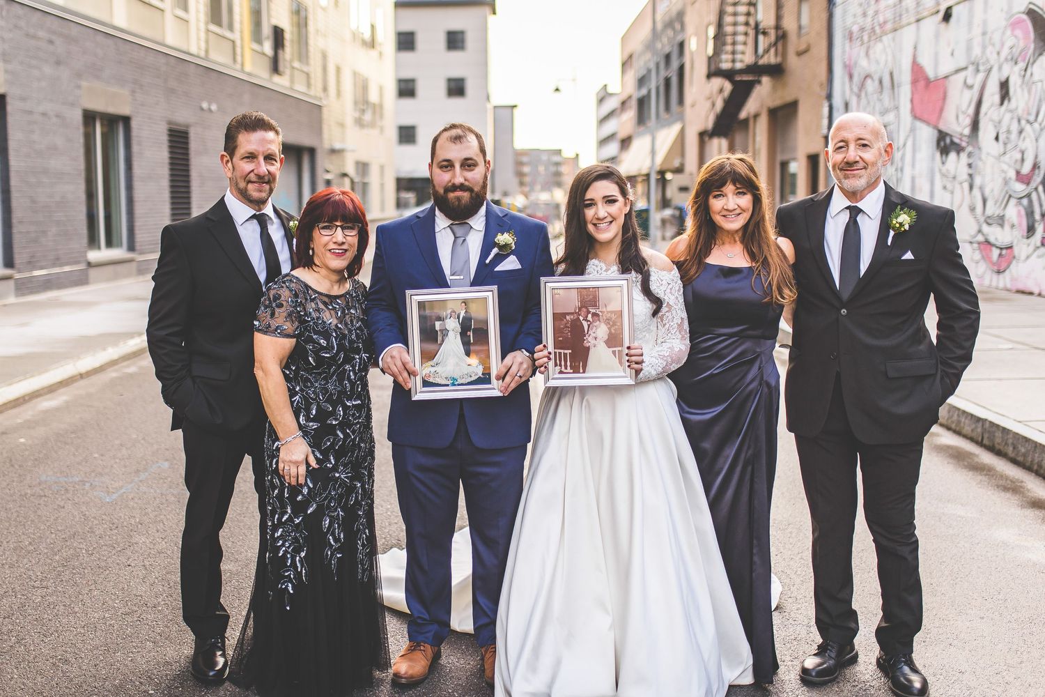 Wedding party lined up for formal photo on city sidewalk with historic architecture.