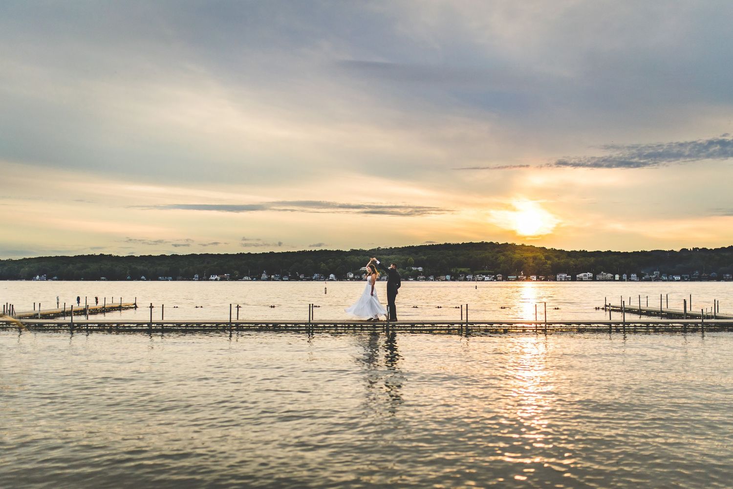 Panoramic view of lake pier and sunset with distant shoreline.