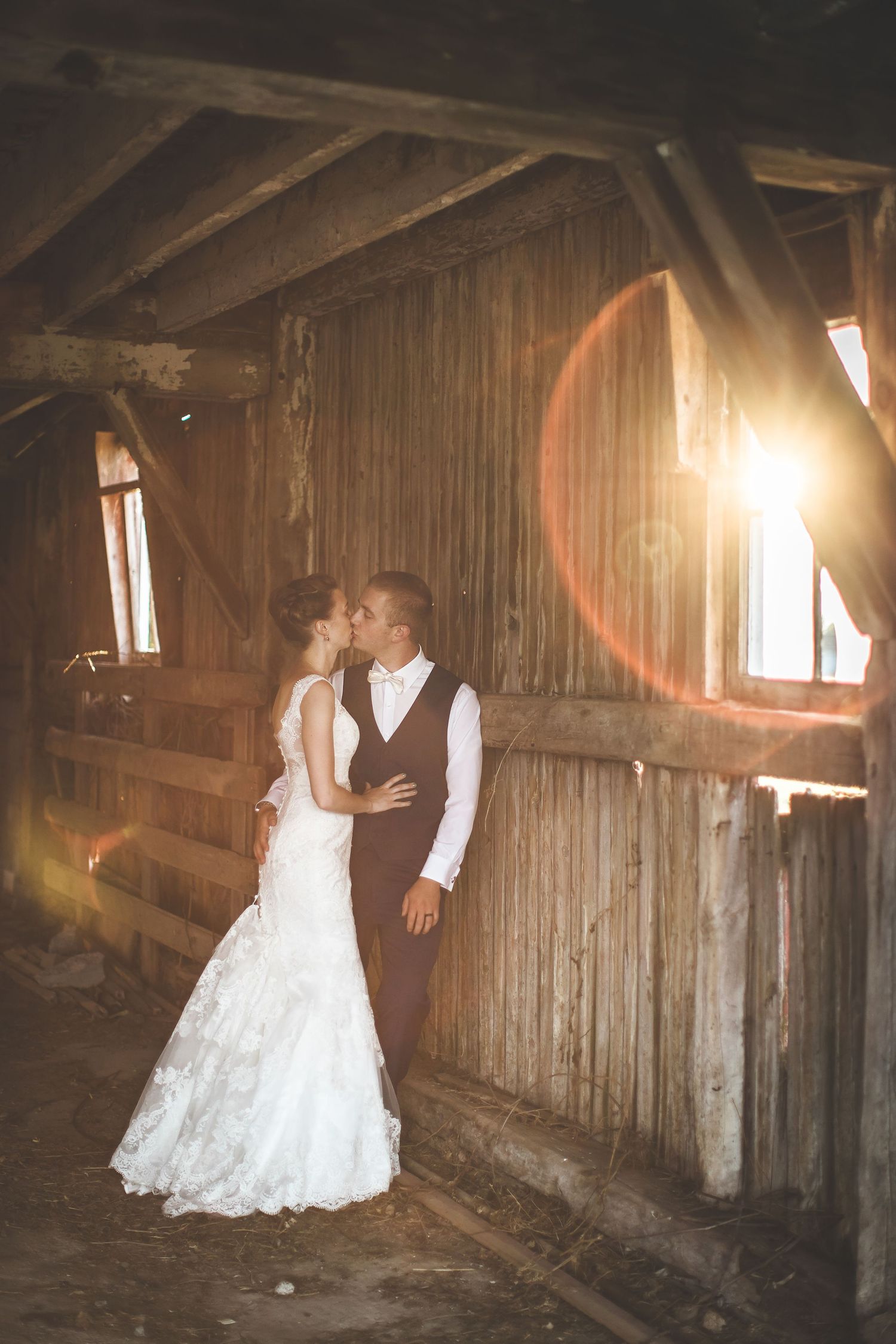 Rustic barn wedding photos with sunlight streaming through wooden slats.