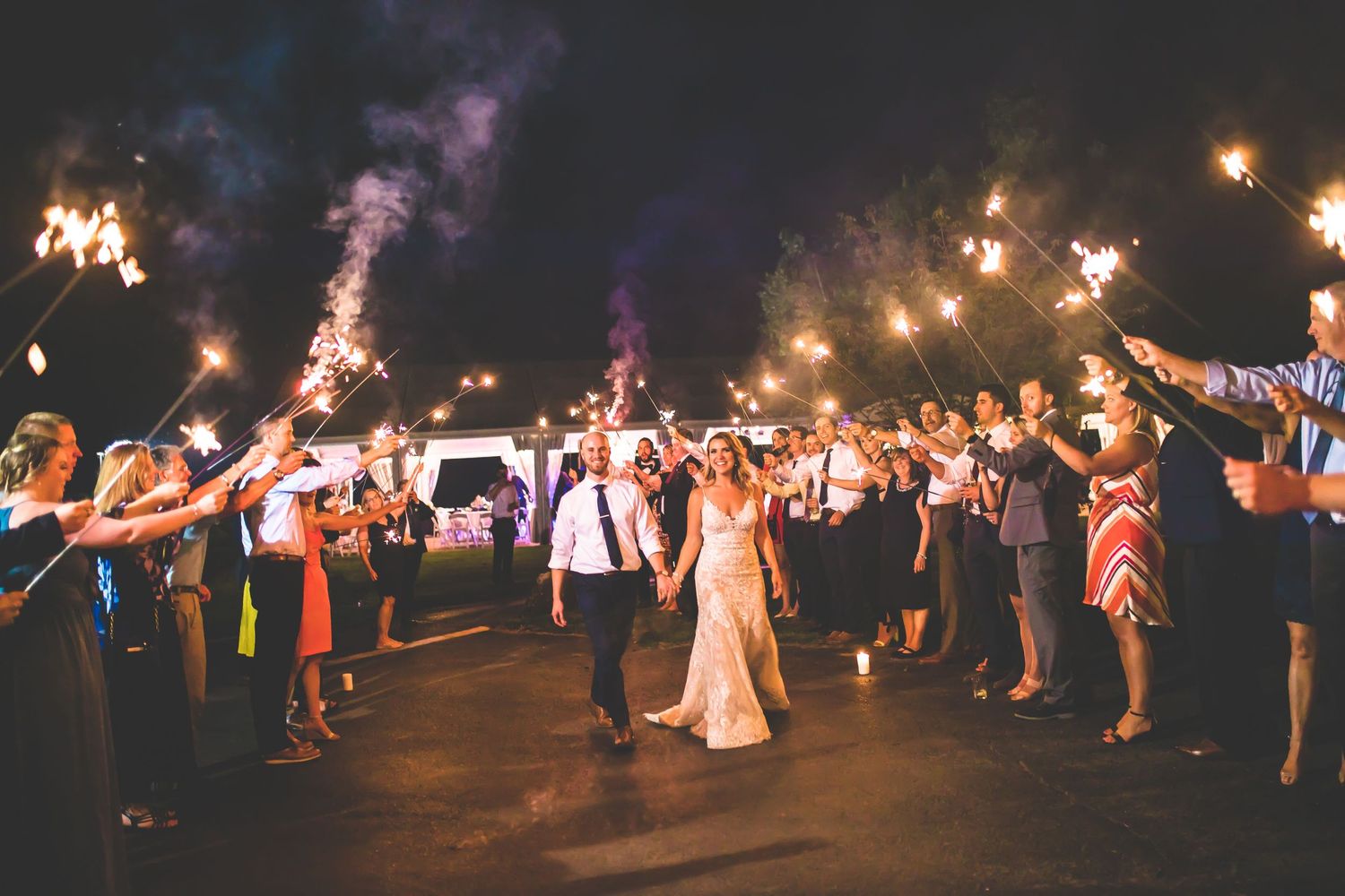 Nighttime wedding celebration with sparklers creating a magical light tunnel effect.