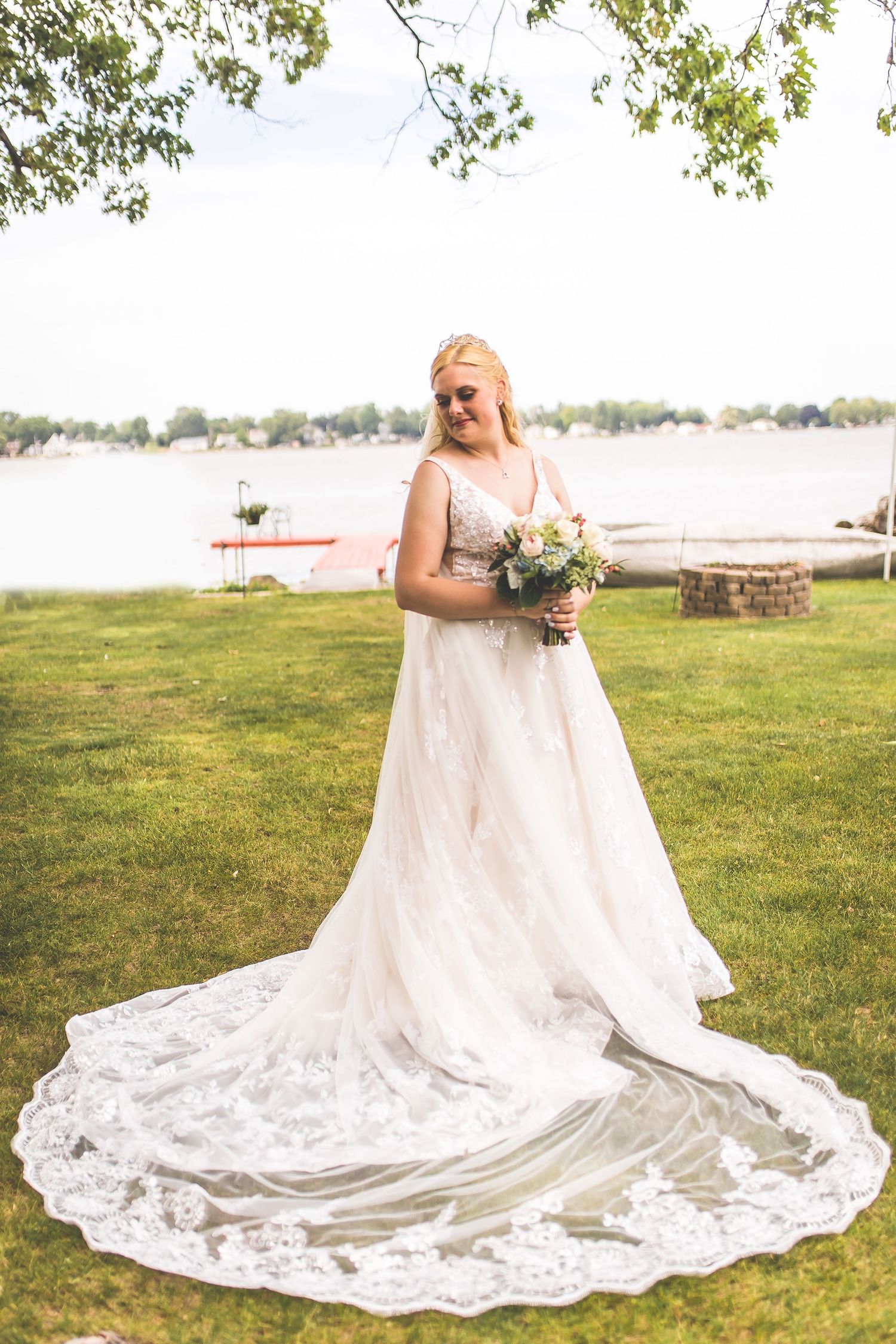 Elegant white lace wedding dress with long train spread out on green grass.