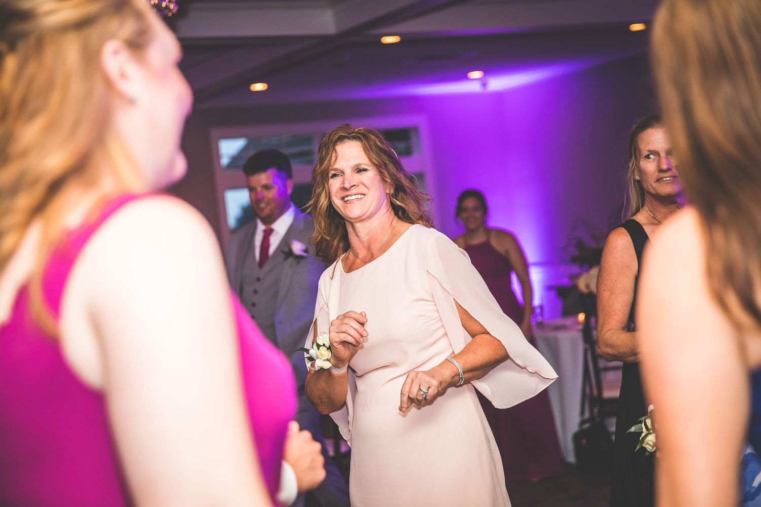 Wedding guests dancing and celebrating at reception with purple ambient lighting.
