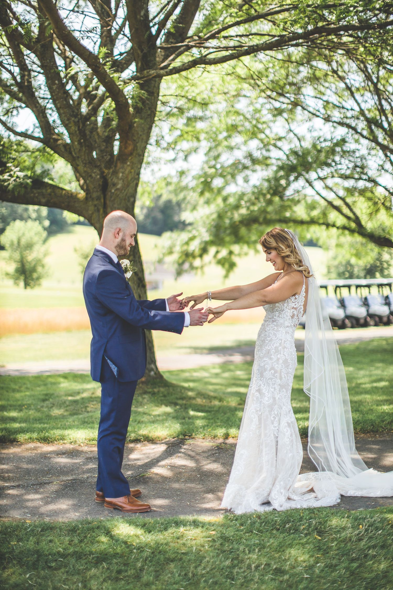 A first look moment between newlyweds under a large tree in a garden setting.