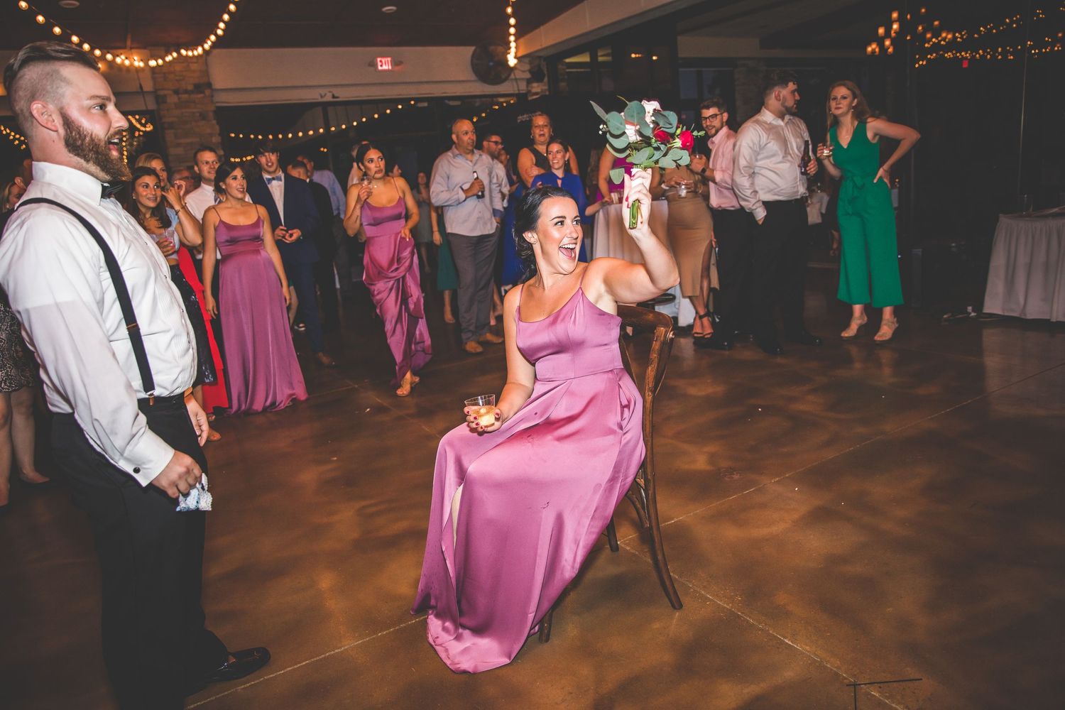 Wedding guests dancing and celebrating on a dimly lit dance floor with string lights overhead.
