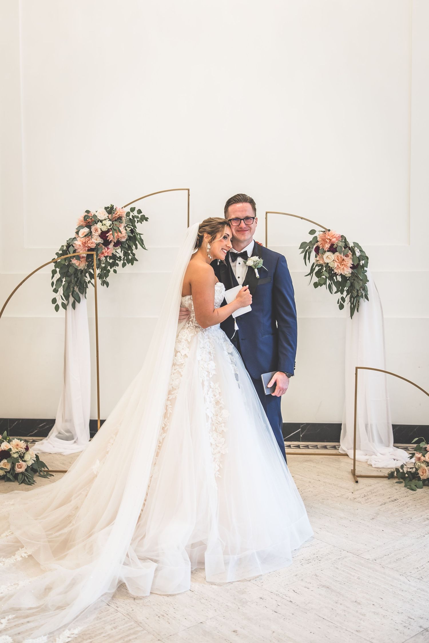 A tender moment between newlyweds under a floral arch during their wedding ceremony.