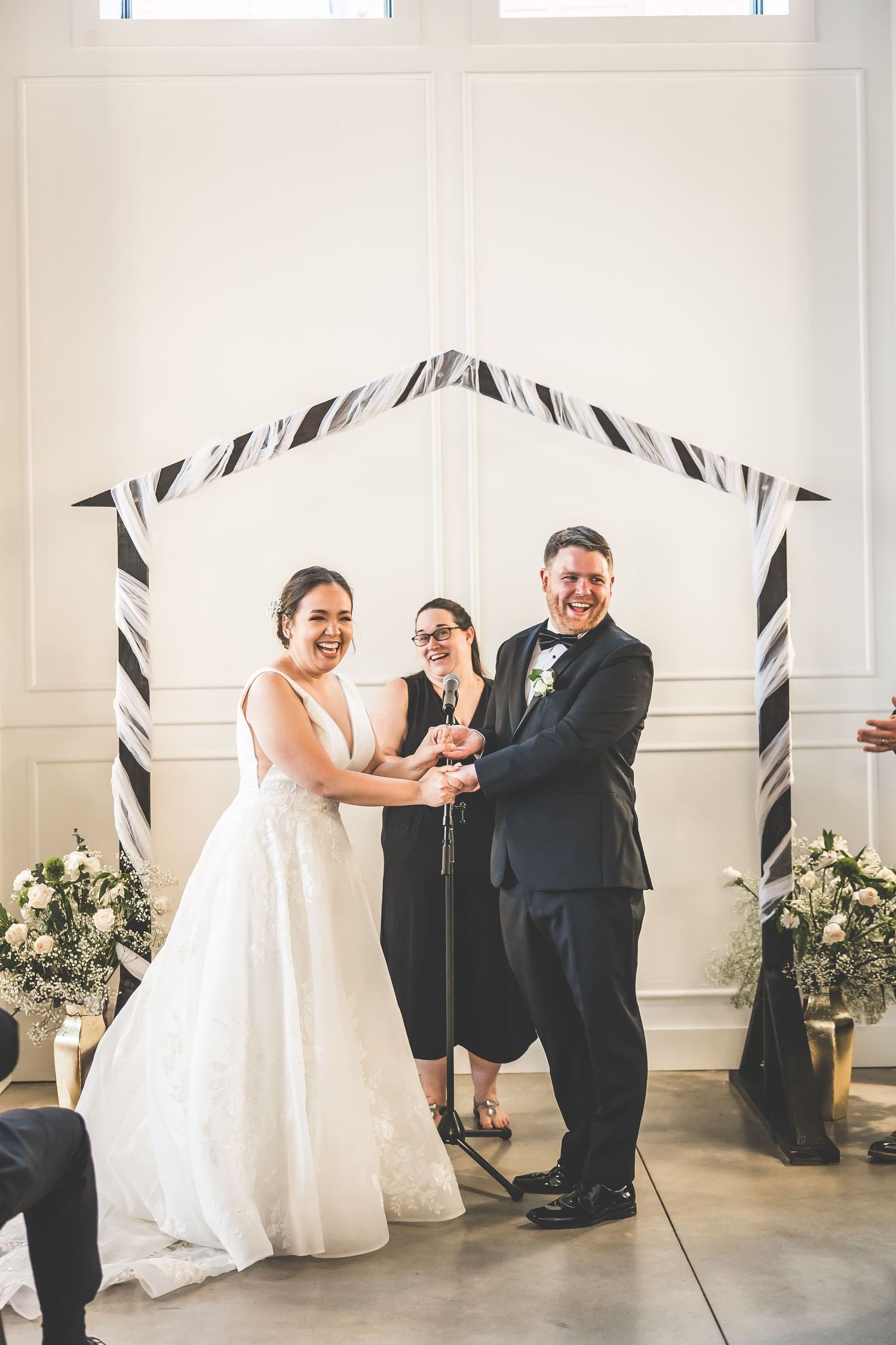 Wedding couple shares a joyful dance with guests at their reception in an elegant white-walled venue.
