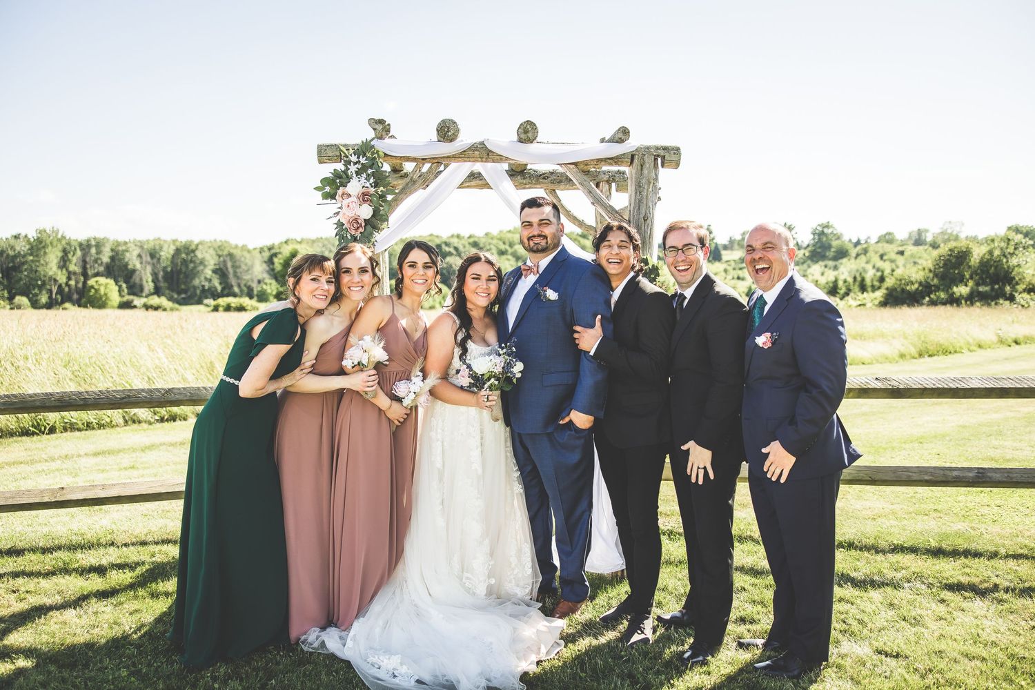 Wedding party in navy and blush tones poses together on sunny outdoor lawn.