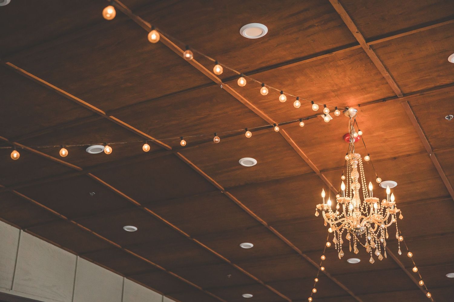 Rustic wooden ceiling with string lights and chandelier creating romantic ambiance.