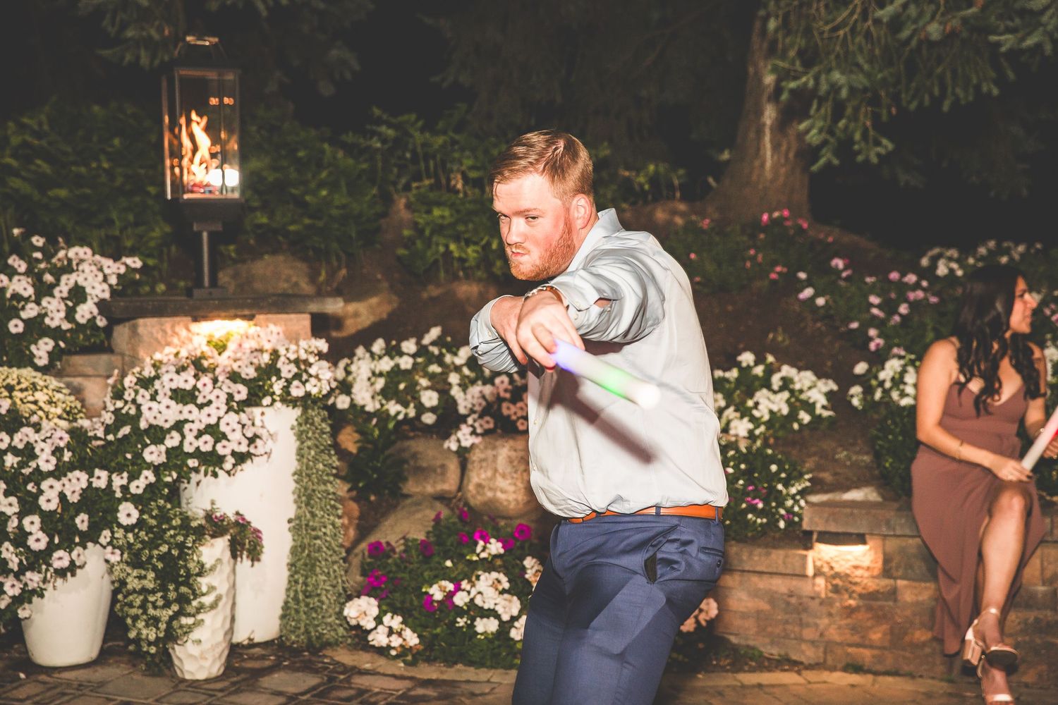 String lights illuminate an outdoor wedding reception area with floral decorations and dancing guests.