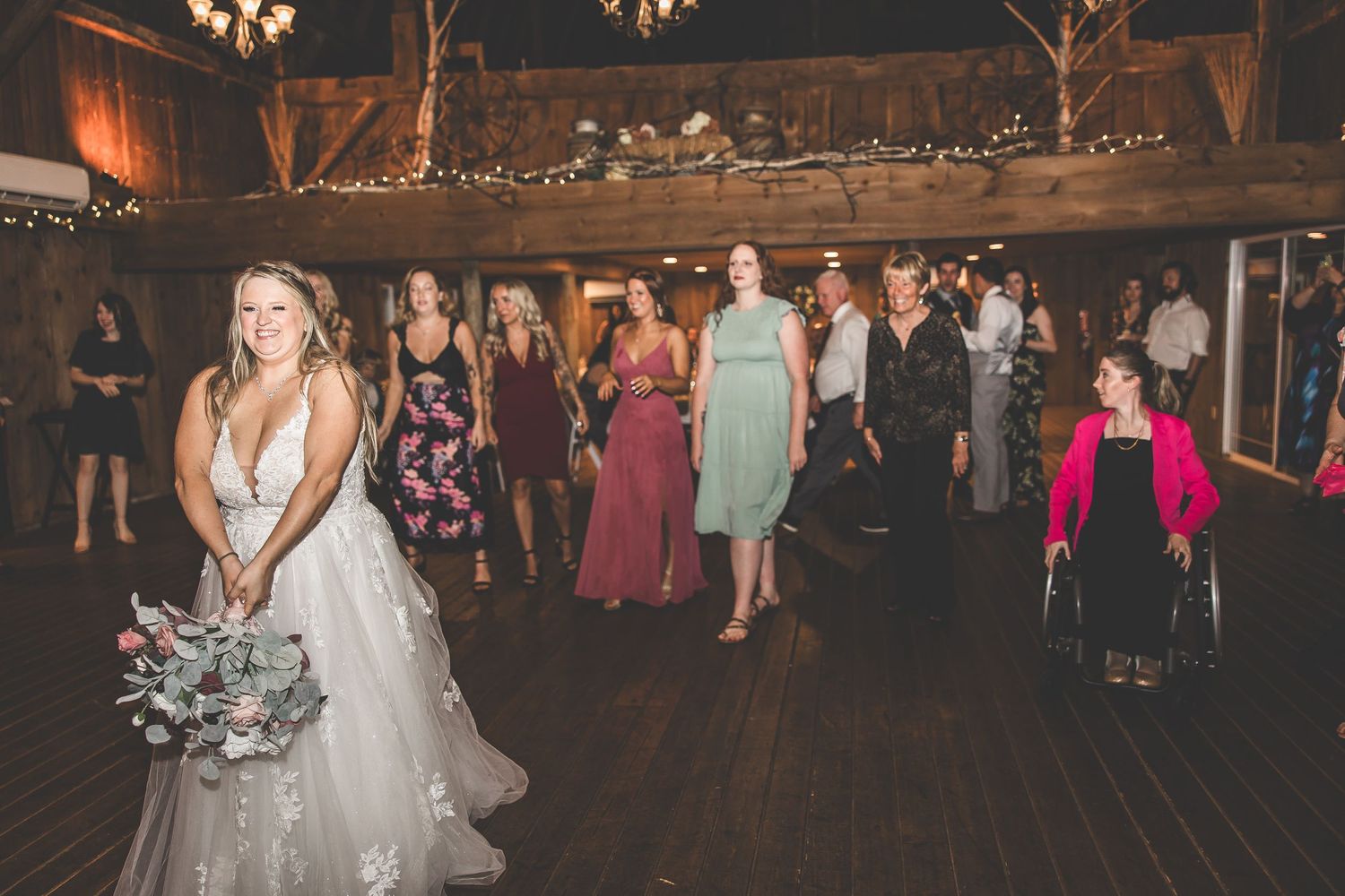 Guests dancing at a wedding reception in a rustic barn venue with twinkle lights decorating the ceiling.
