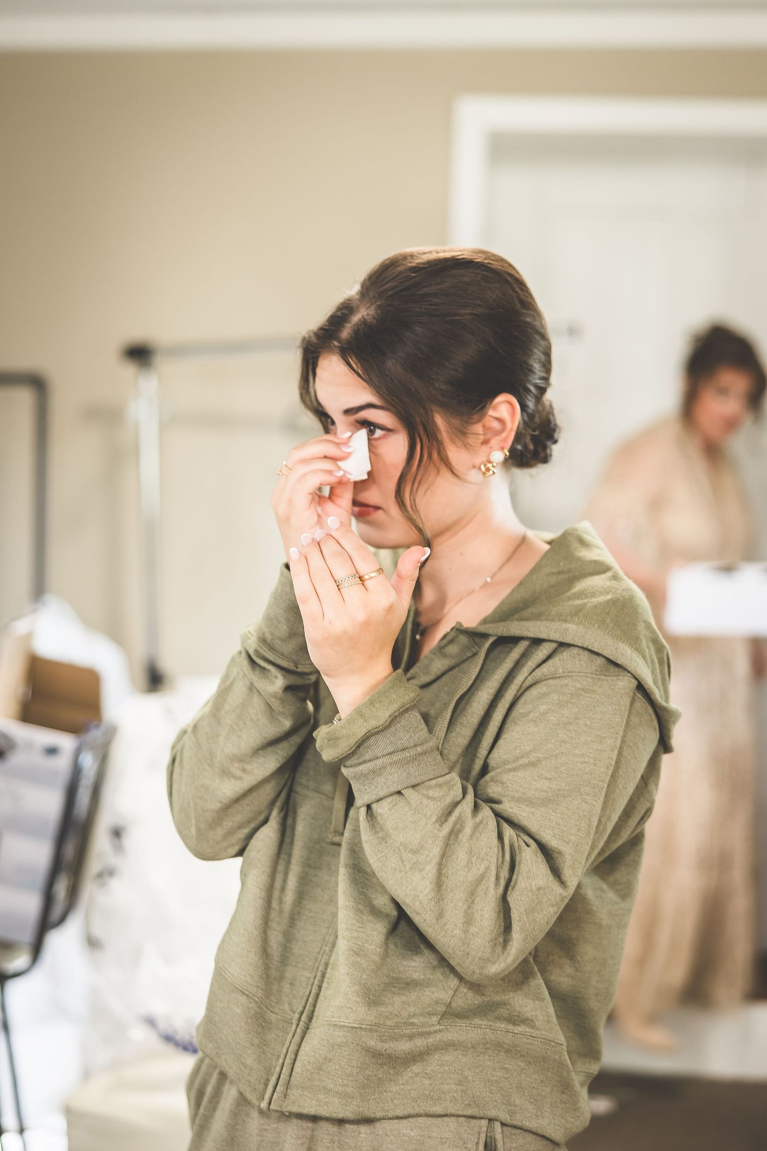 Person in olive green hoodie shows emotional reaction with hands covering face.