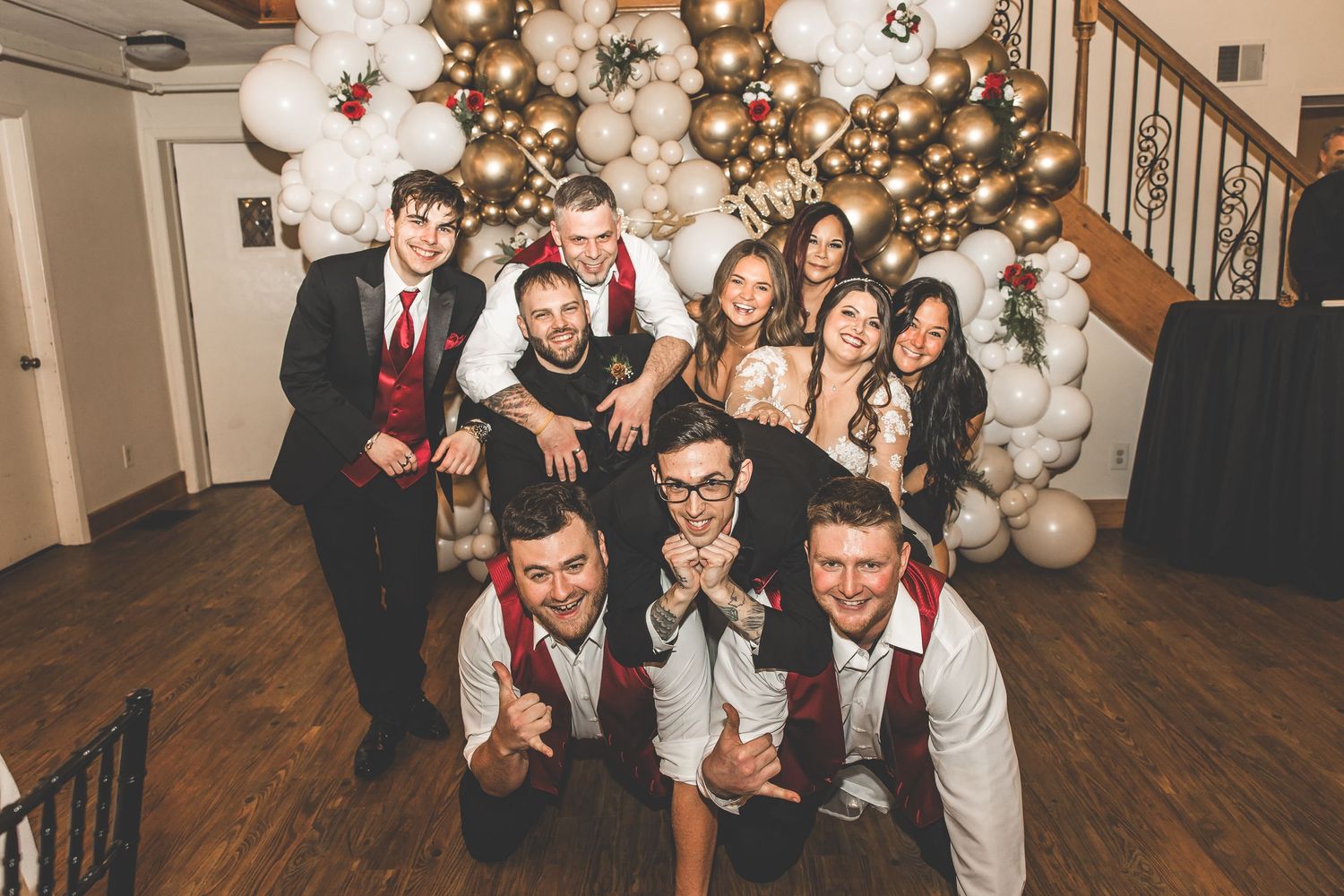 Wedding party poses near a decorated Christmas tree with gold and white balloon arrangements.