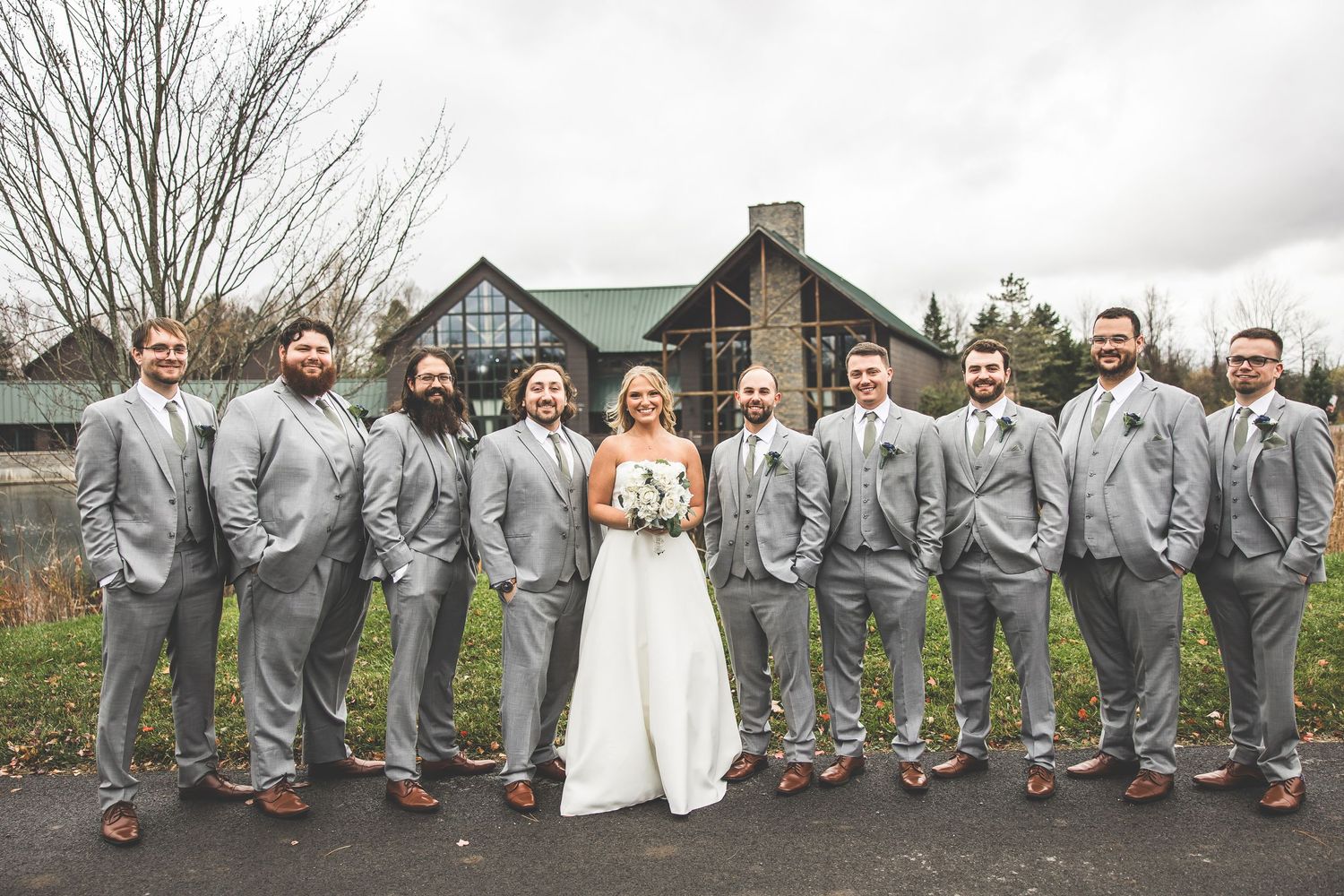 Bridal party with navy dresses and gray suits poses together on rustic outdoor grounds.