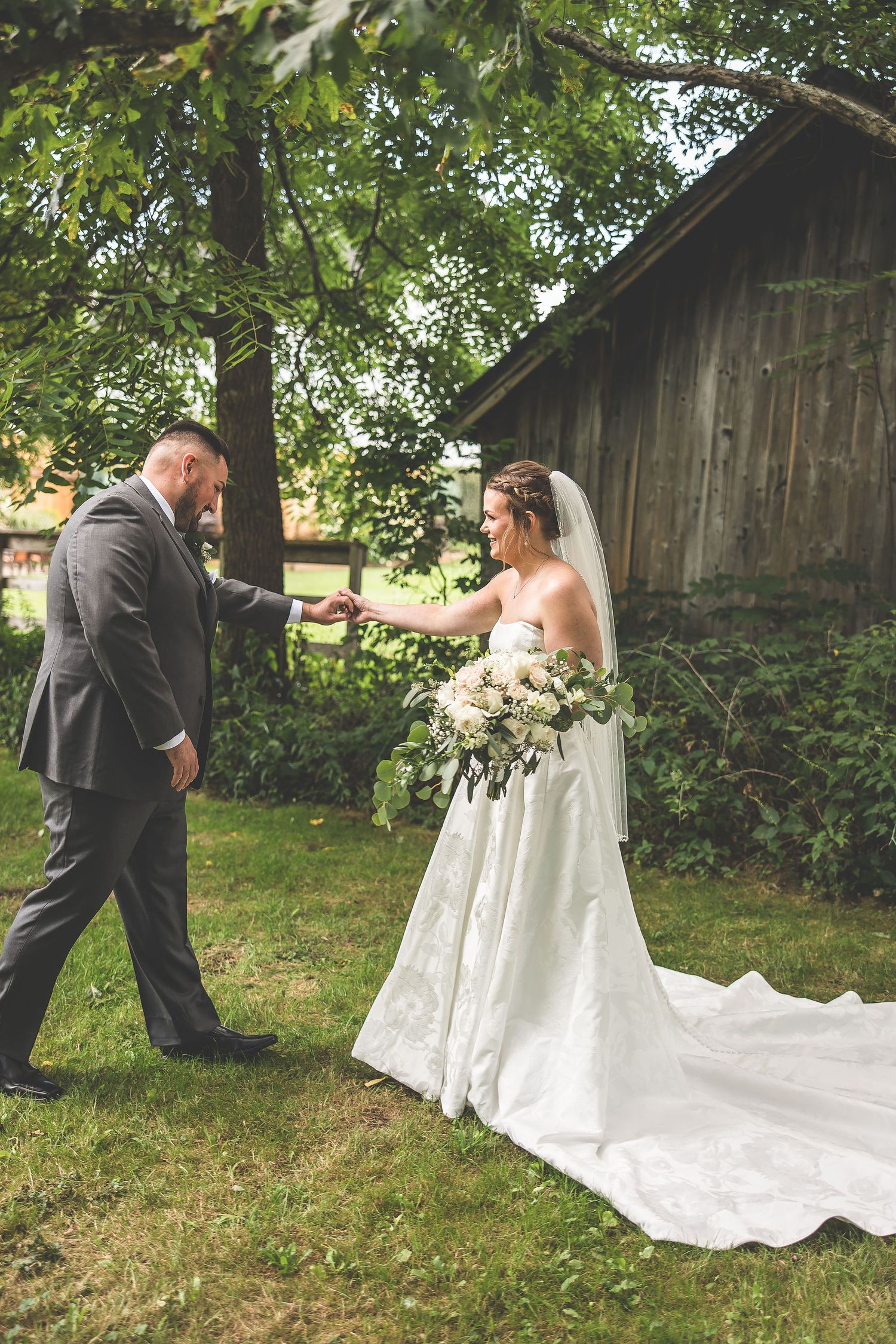 Candid wedding moments photographed near vintage barn with dramatic dress train.