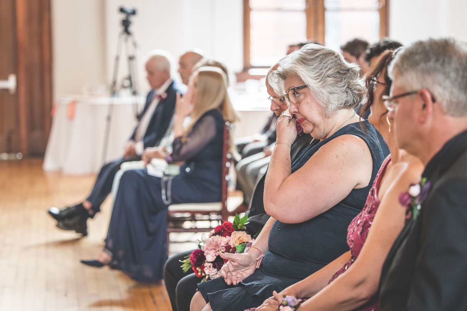 Wedding guests seated in rows watching ceremony in bright sunlit venue.