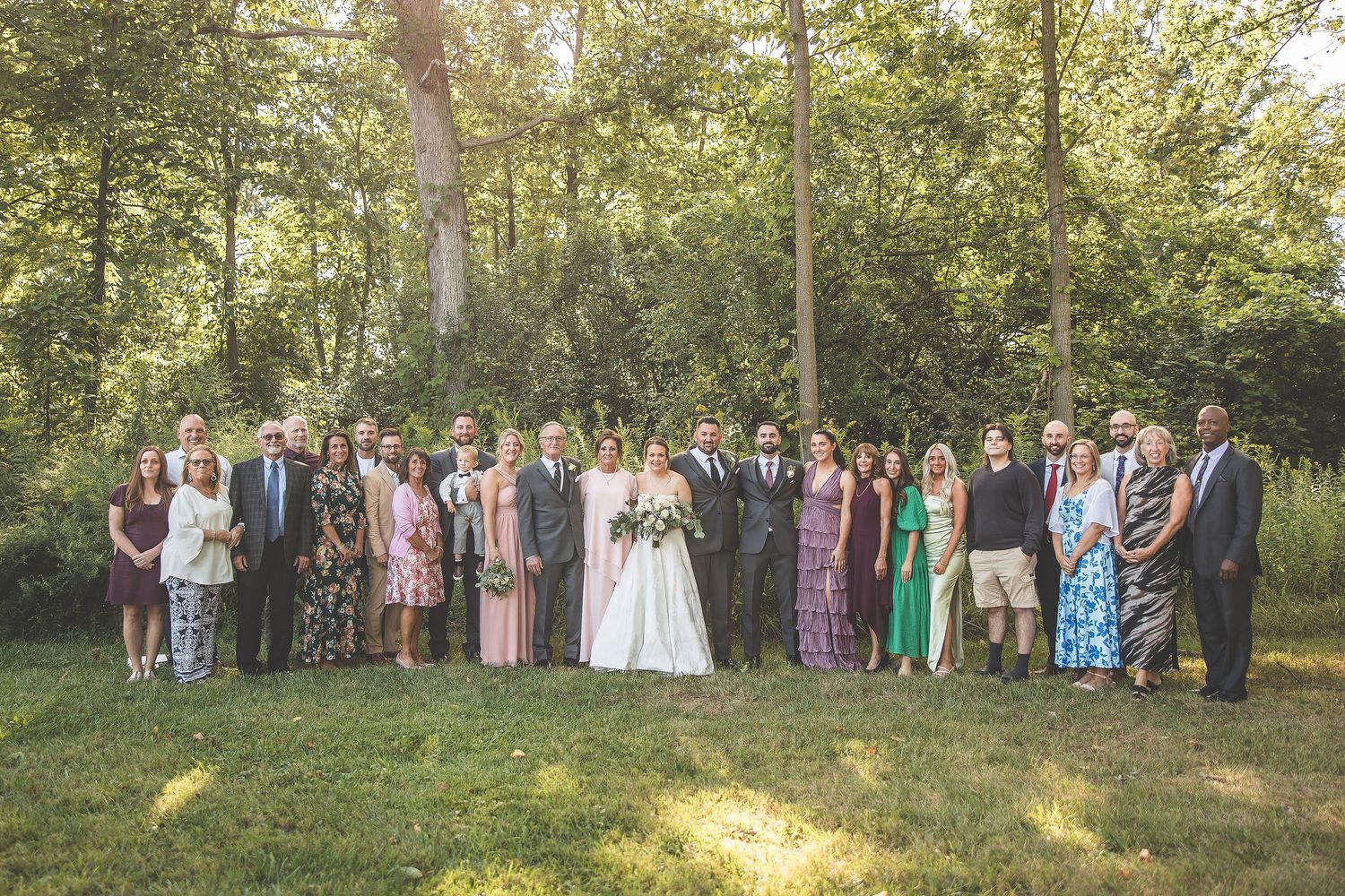 Wedding party and guests lined up for formal group photos in an outdoor garden setting.