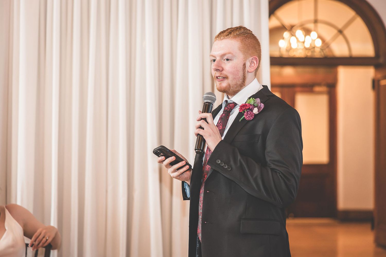 A wedding speech being delivered in front of white curtains at an elegant venue.