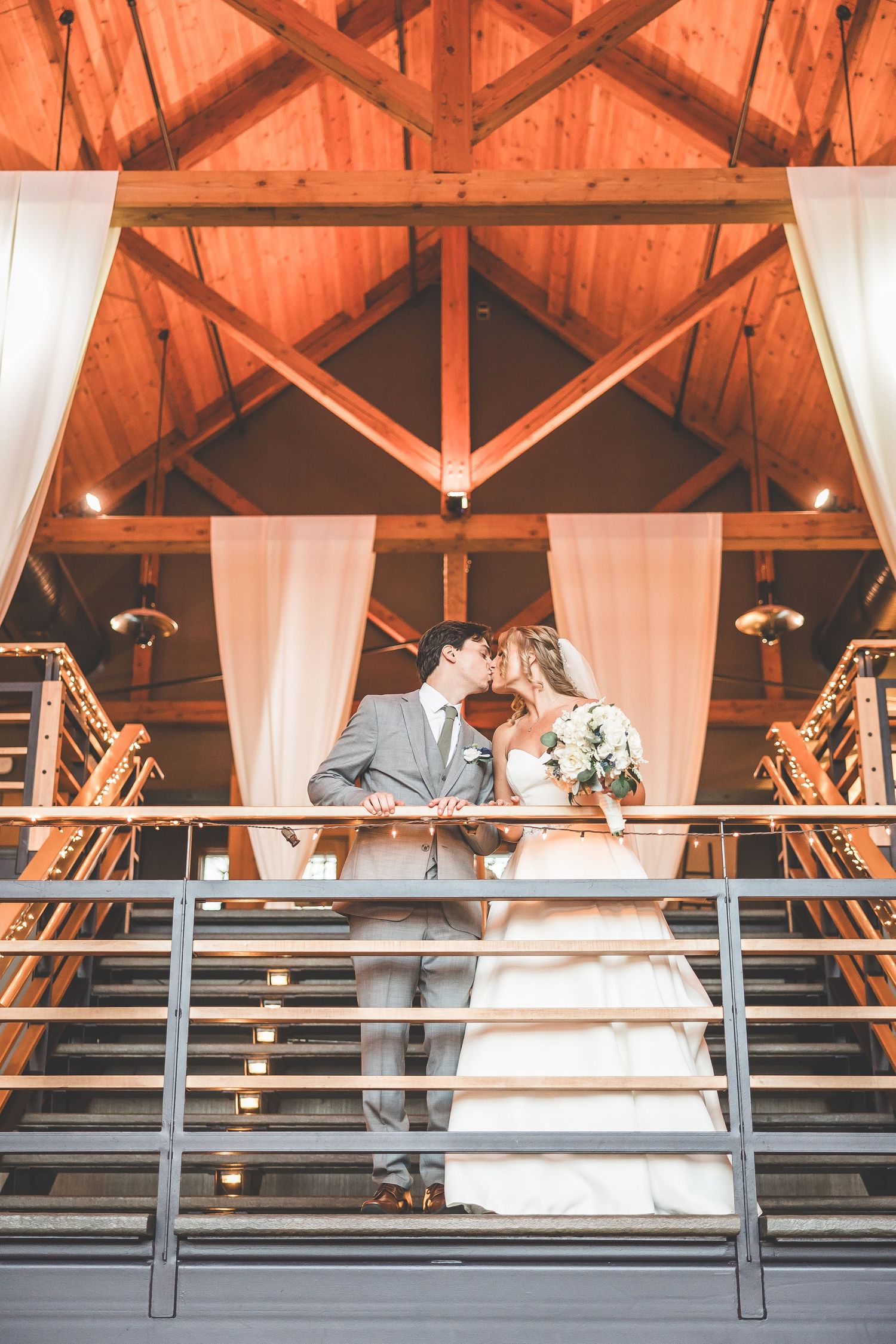 Wedding couple on balcony with exposed wooden beams and white draping in warm lighting.