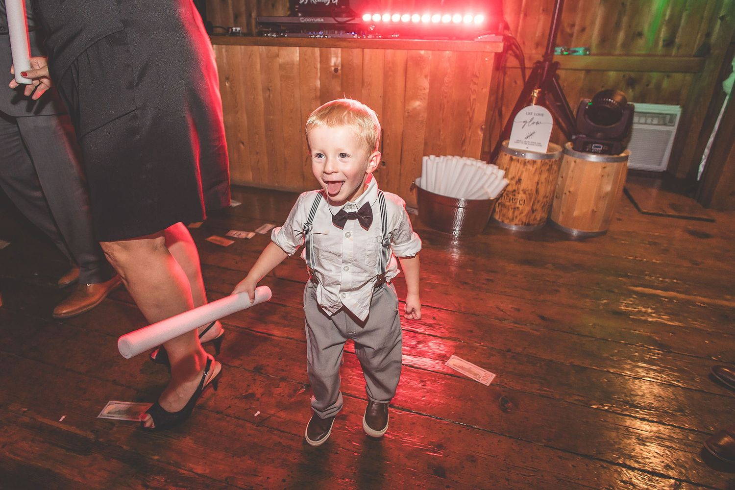 Wedding guests dance energetically on a rustic wooden dance floor illuminated by red lighting.