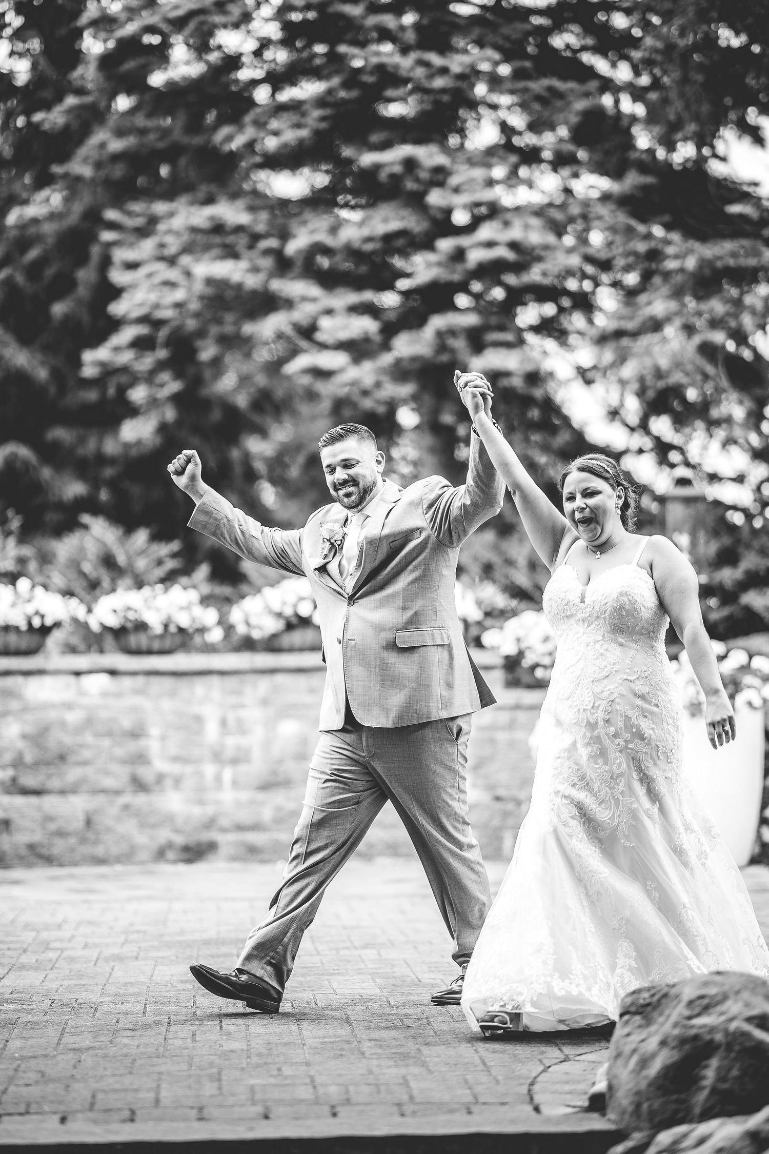 A playful black and white sequence of a wedding couple dancing and celebrating on brick pavement.