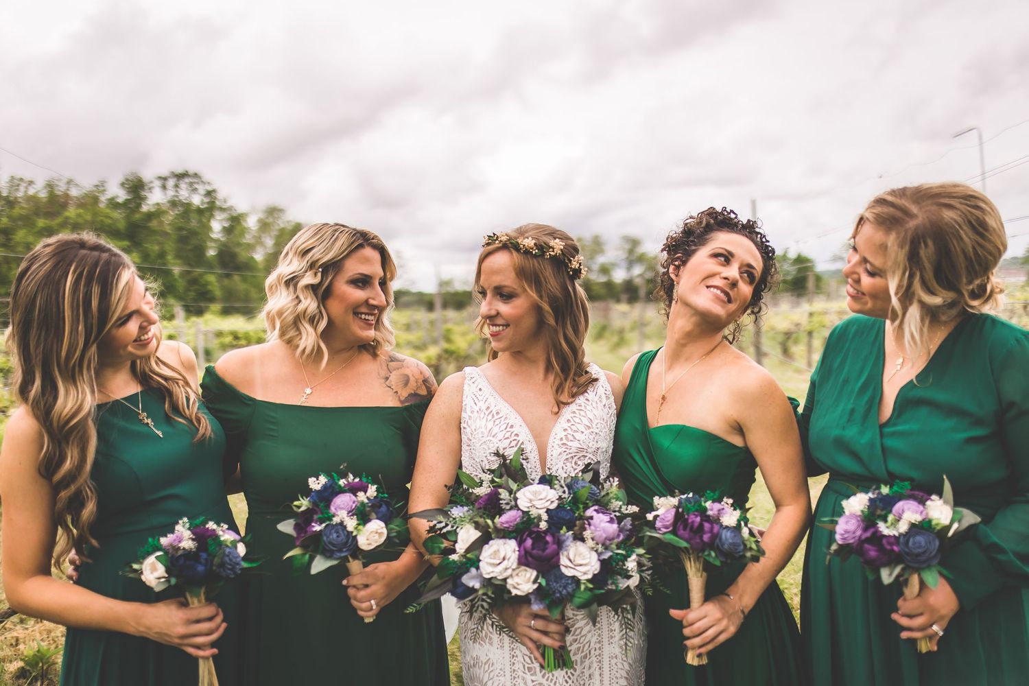 Wedding party laughs together while posing in vineyard with green and white color scheme.