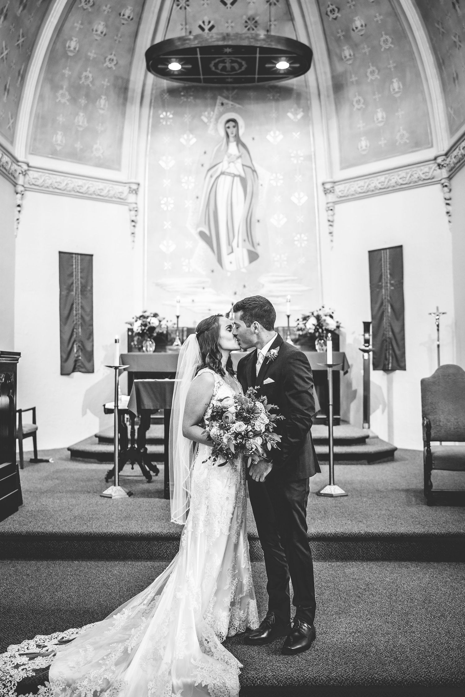 Black and white wedding photos captured in ornate church sanctuary with patterned ceiling.