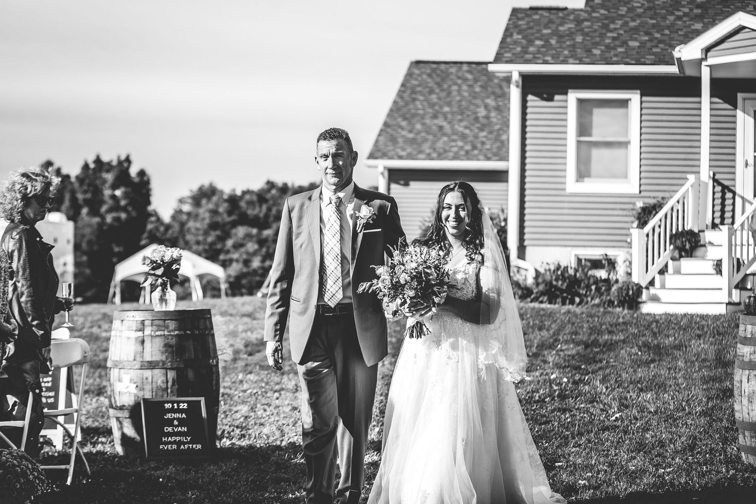 Black and white photo of couple walking down aisle at outdoor ceremony.