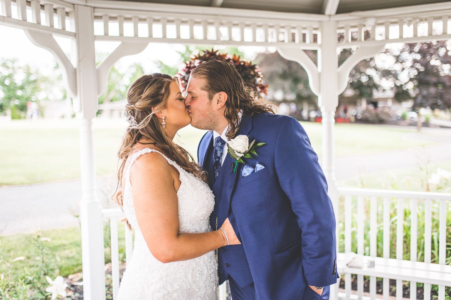 A romantic first kiss between newlyweds under a white gazebo during their wedding ceremony.