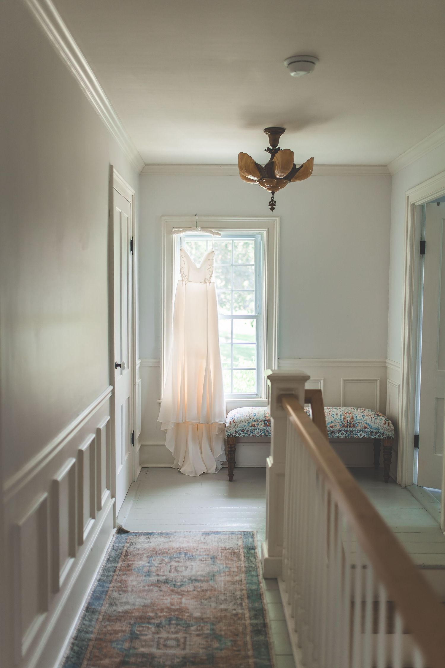 Interior hallway with white walls, vintage runner carpet, and natural light streaming through windows.
