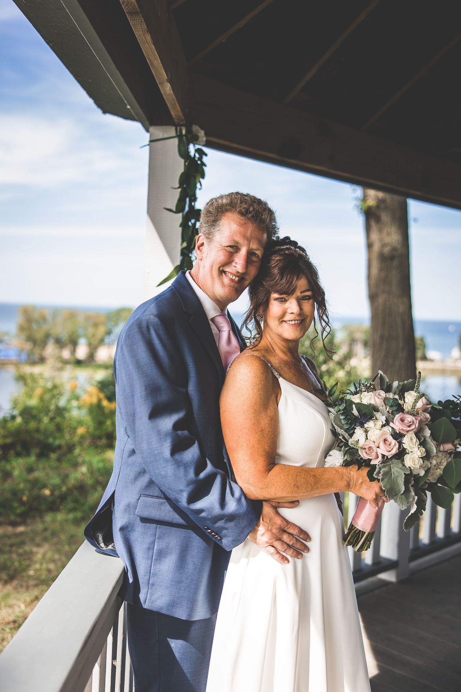 Wedding couple poses for romantic photos on a covered deck with scenic views.